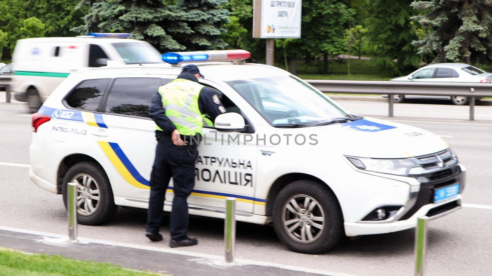 Ukraine, Kiev - June 2, 2020. Police patrol cars provide safety on the roads of Kiev in Ukraine. A male policeman stands near his car on the roadway.