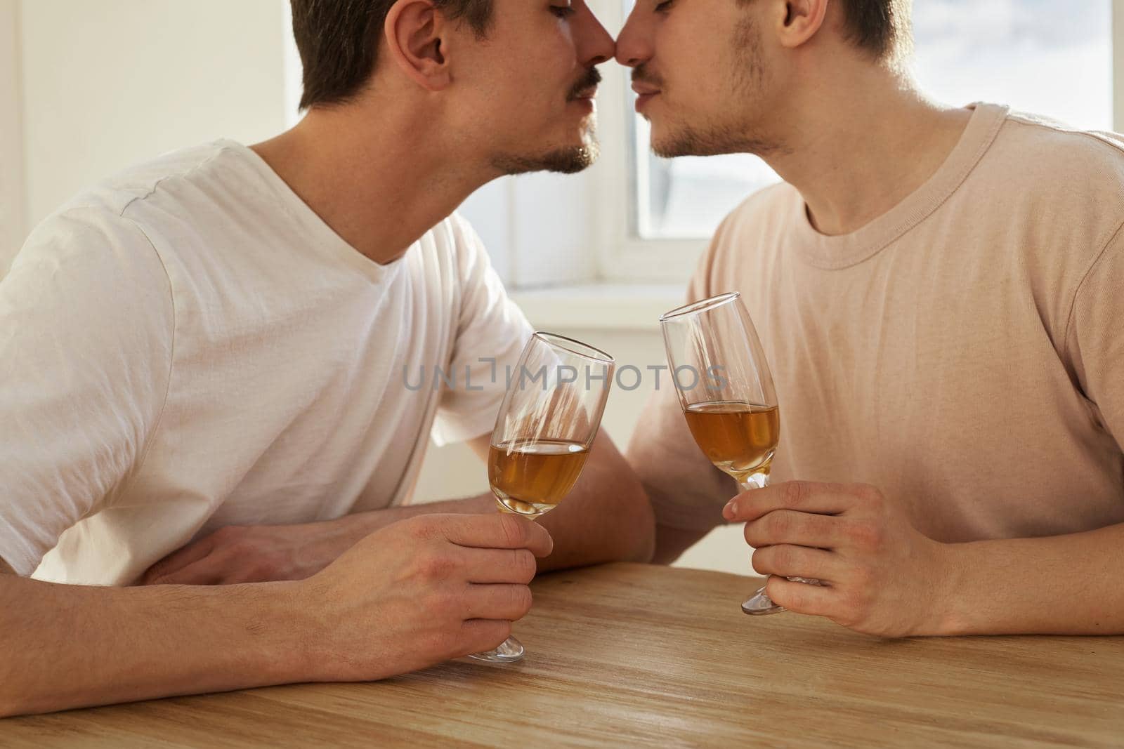Gay couple of men drink wine from glasses and kiss at home