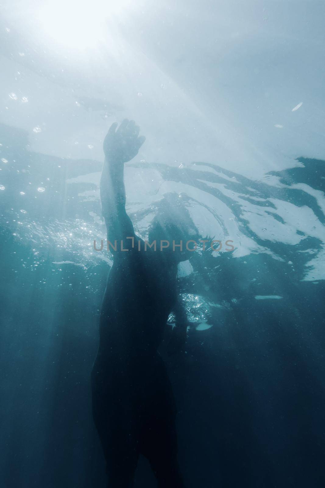 Freediver young man swimming underwater among sunbeams and using crawl technique.