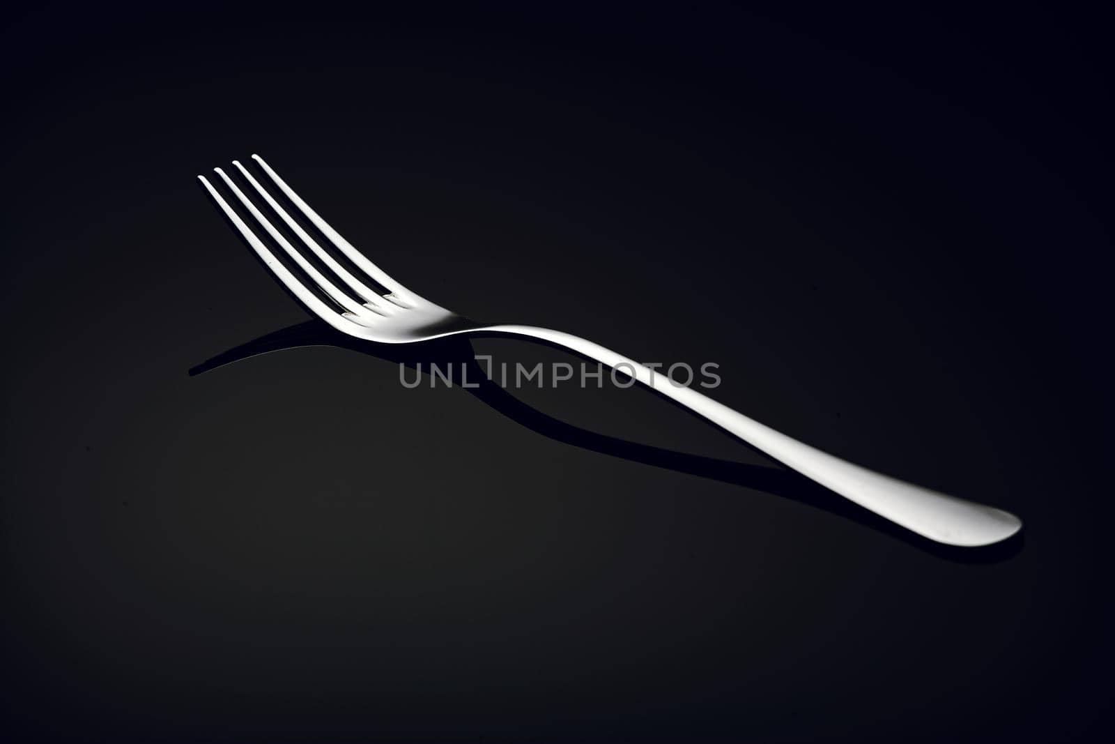 A white metal fork lies on a black glass with a reflection. A simple kitchen item for advertising.