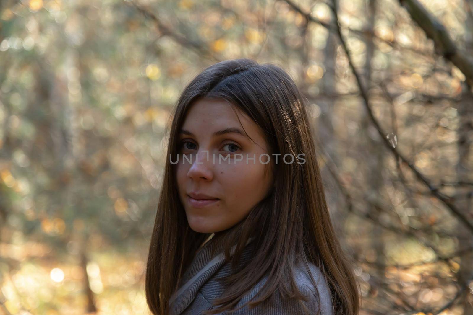 Half-turned girl in a gray coat, which stands in the forest on a sunny autumn day