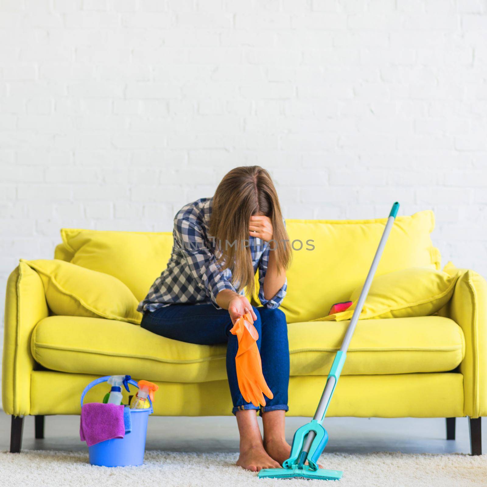 frustrated young woman sitting sofa with cleaning equipments