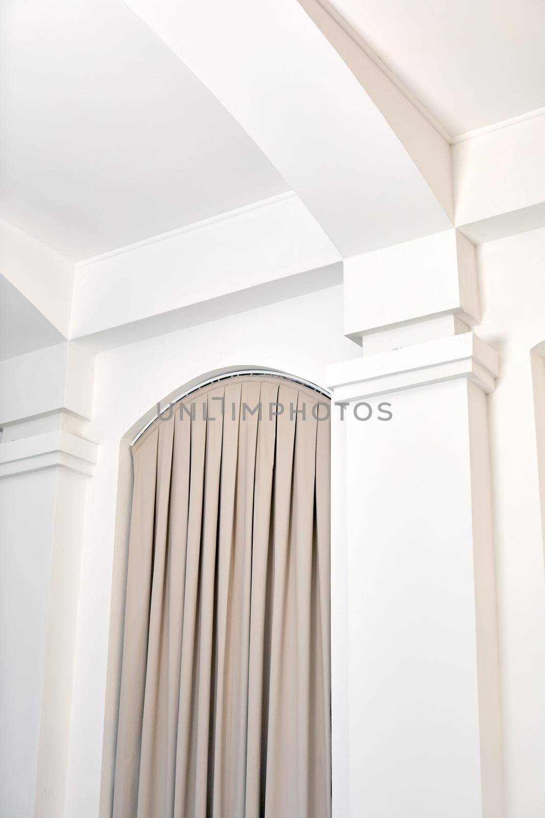 From below of house interior details with white walls and columns and beige curtains