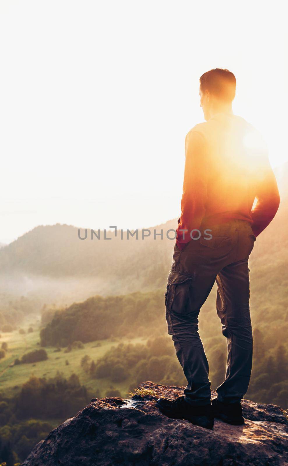 Traveler explorer young man standing on peak of cliff at sunset and enjoying view of nature in summer.