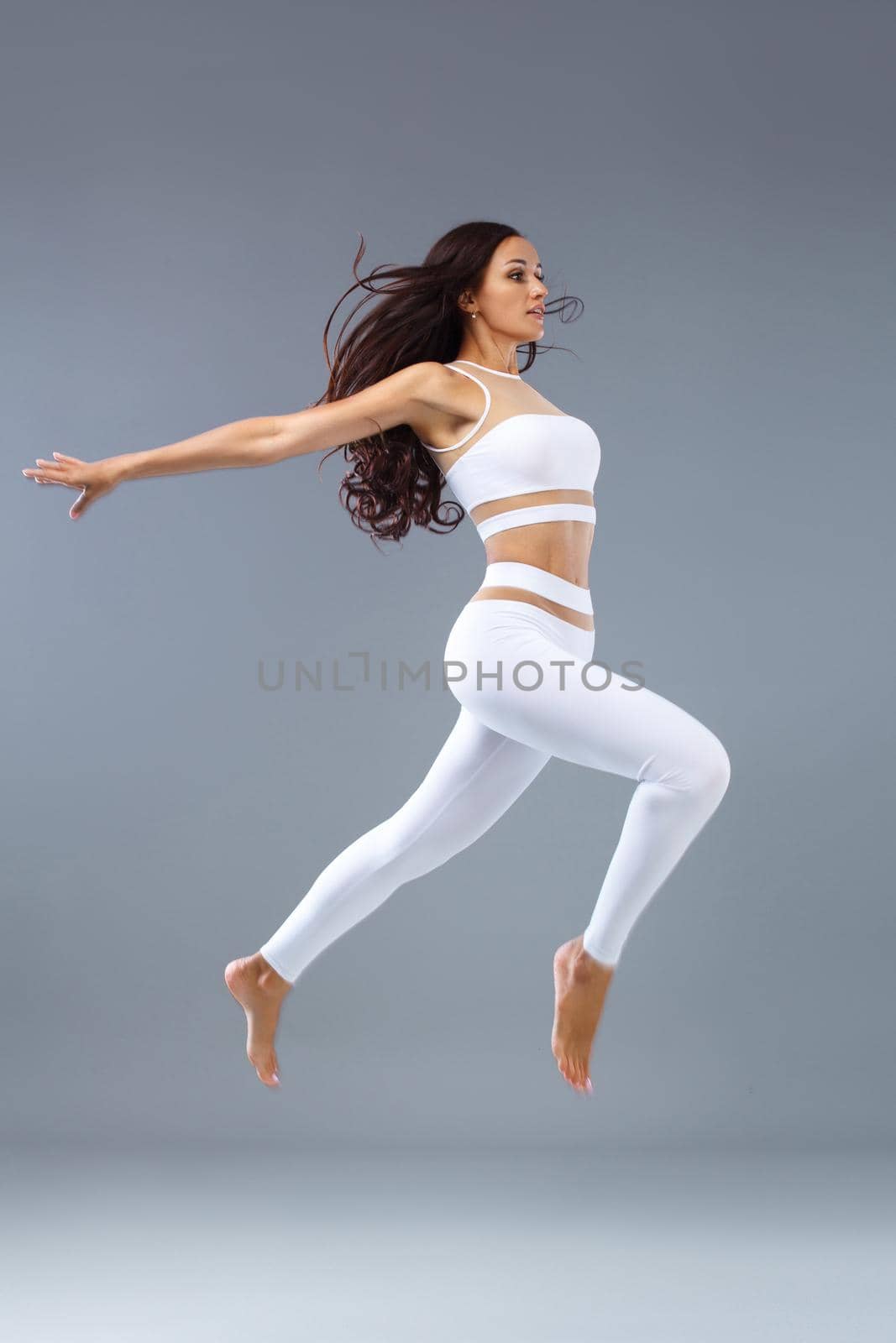 Attractive excited fitness girl in sportwear jumping of joy isolated over light background