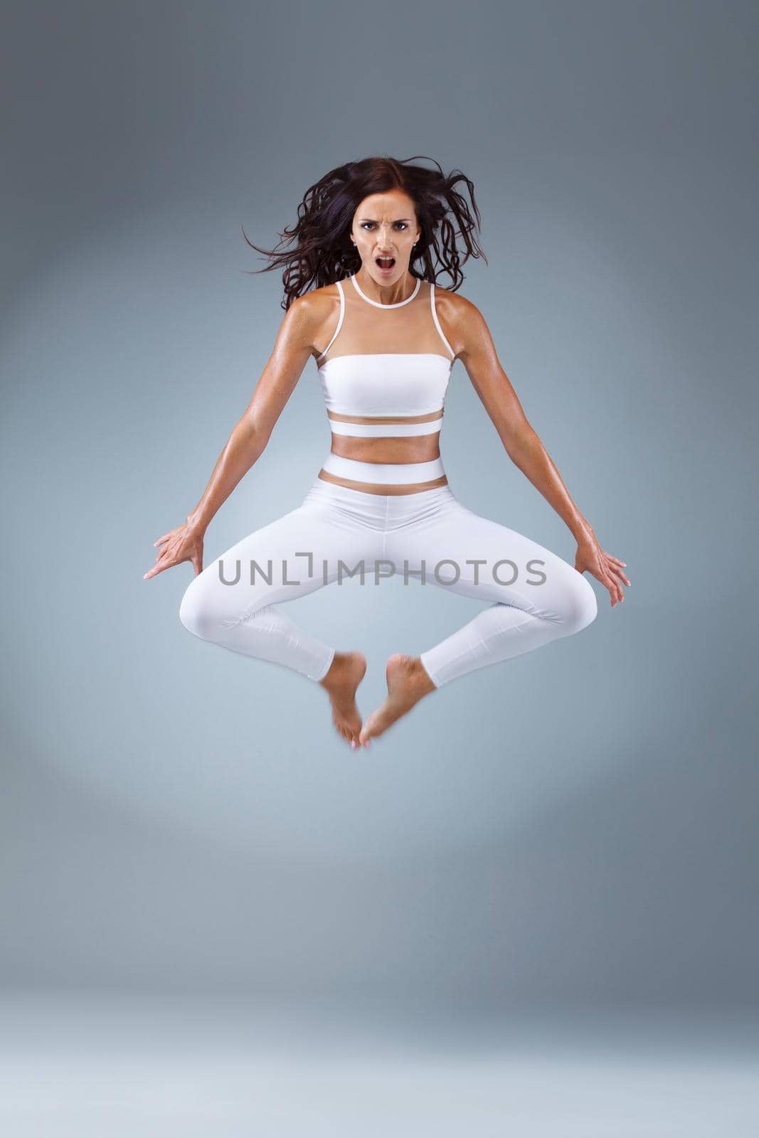 Attractive excited fitness girl, ballerina dancer in sportwear jumping of joy isolated over gray background. by MikeOrlov