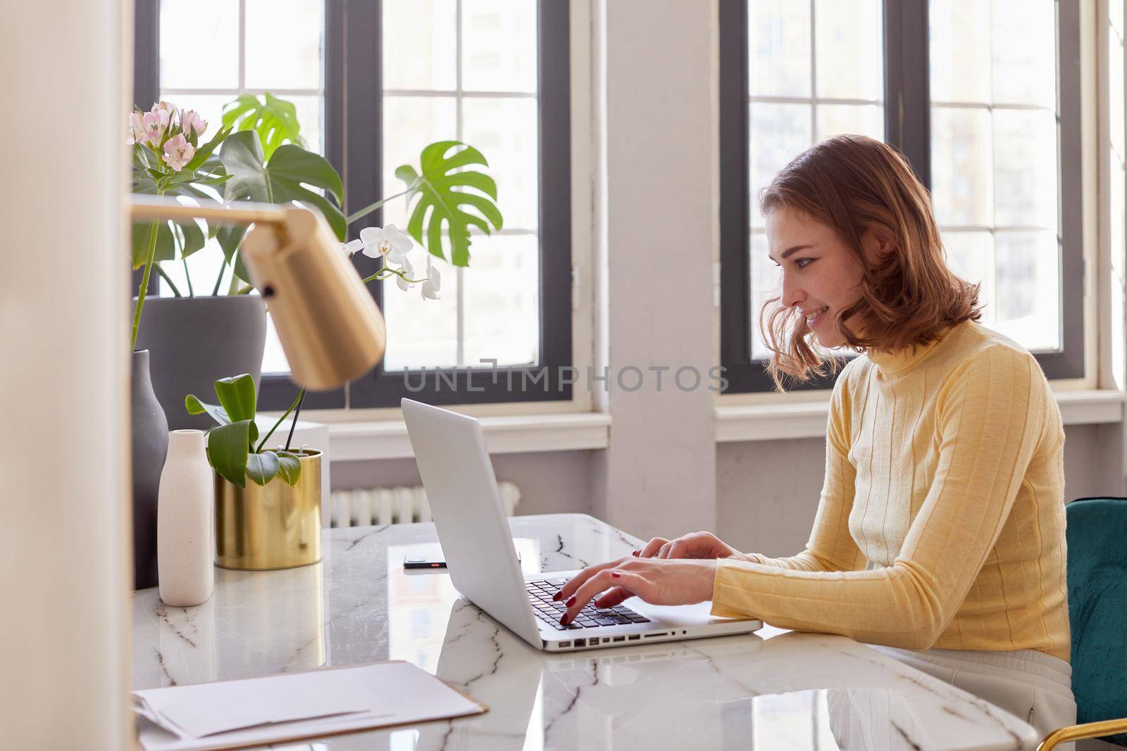 Business woman in yellow turtleneck using laptop computer and sitting by the table in home office