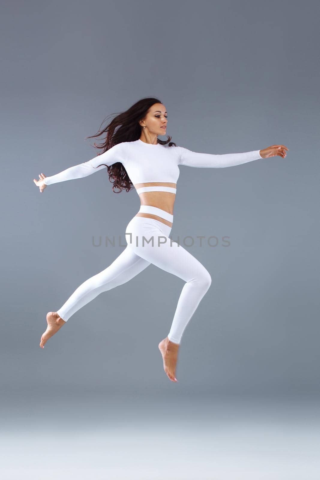 Attractive excited fitness girl, ballerina dancer in sportwear jumping of joy isolated over gray background. by MikeOrlov