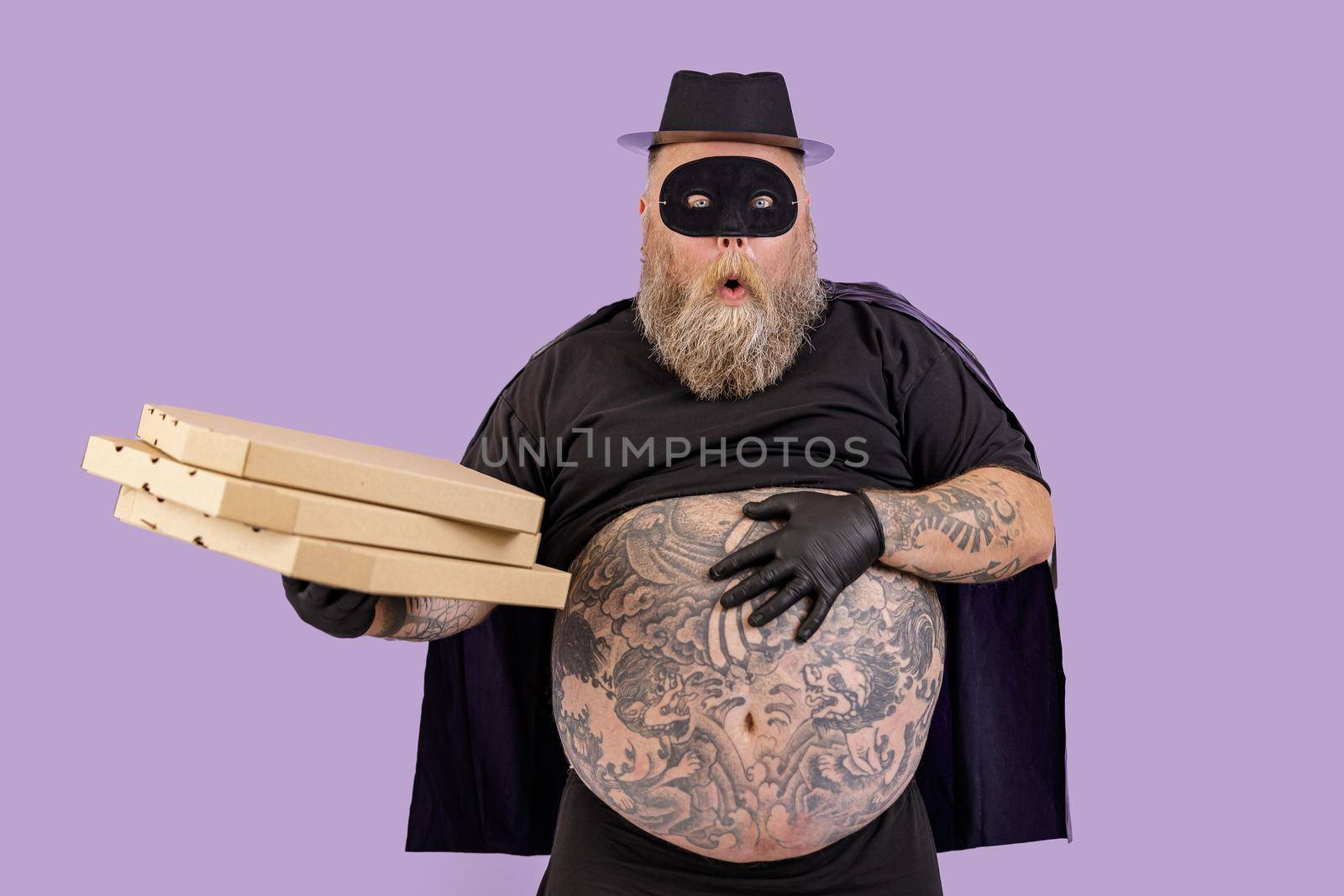 Surprised plump person in Zorro suit holds boxes of pizza on purple background by Yaroslav_astakhov
