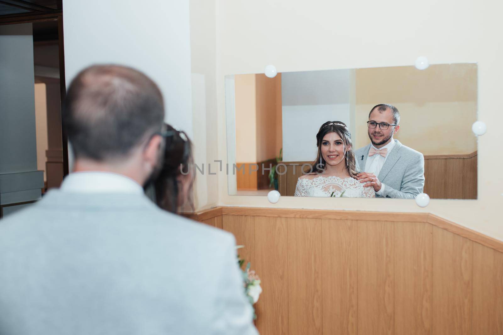 Bride and groom hug and look in their reflection in the mirror by lunarts