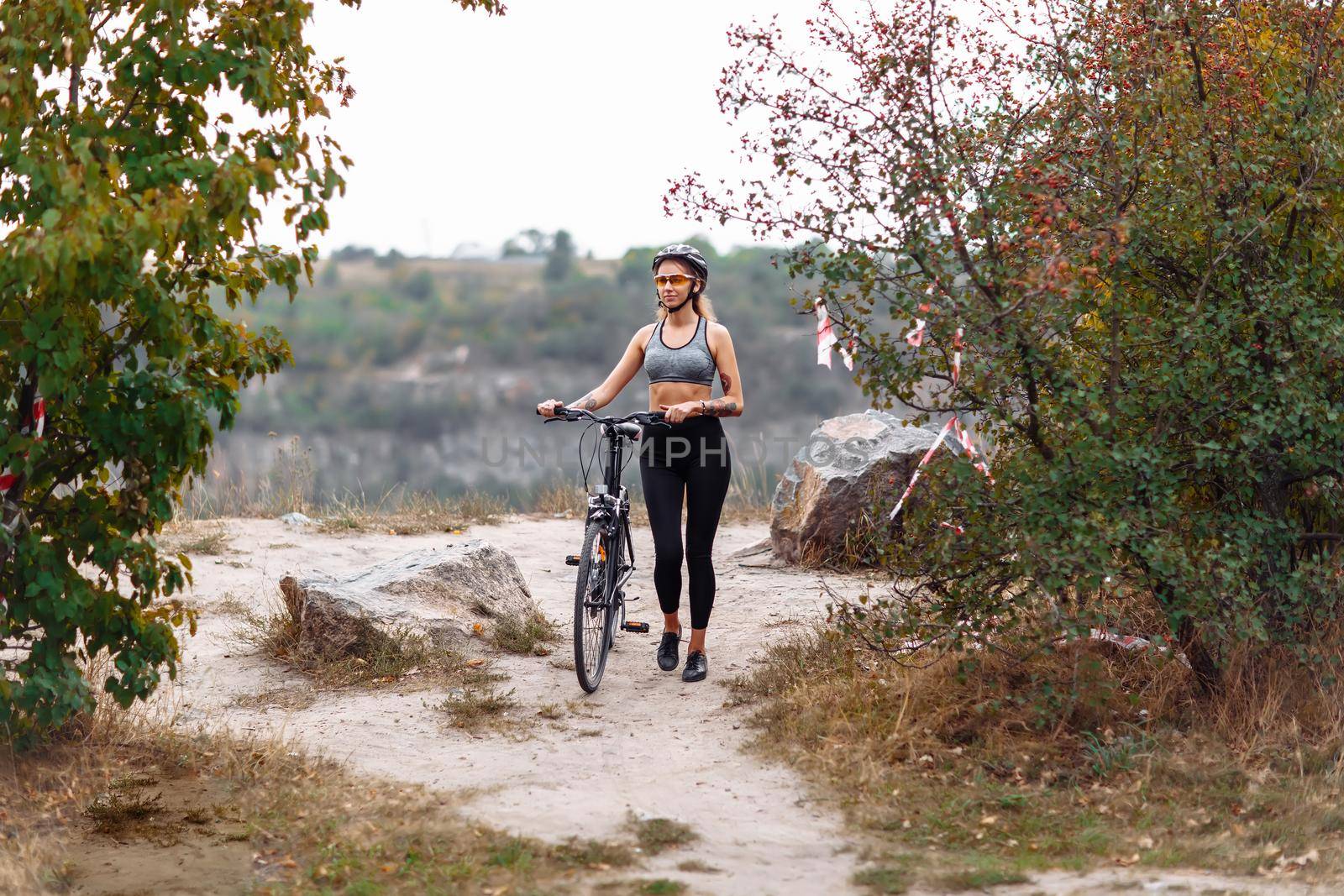 Fit young woman wearing sportswear standing with her bicycle on rocky background at autumn day