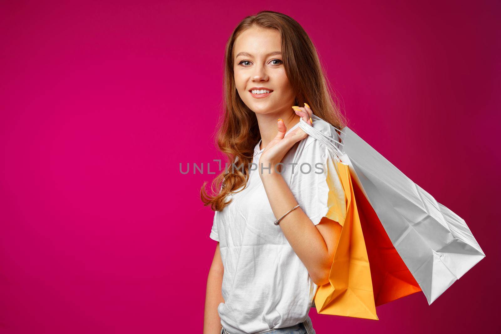 Portrait of happy young smiling woman with shopping bags against pink background