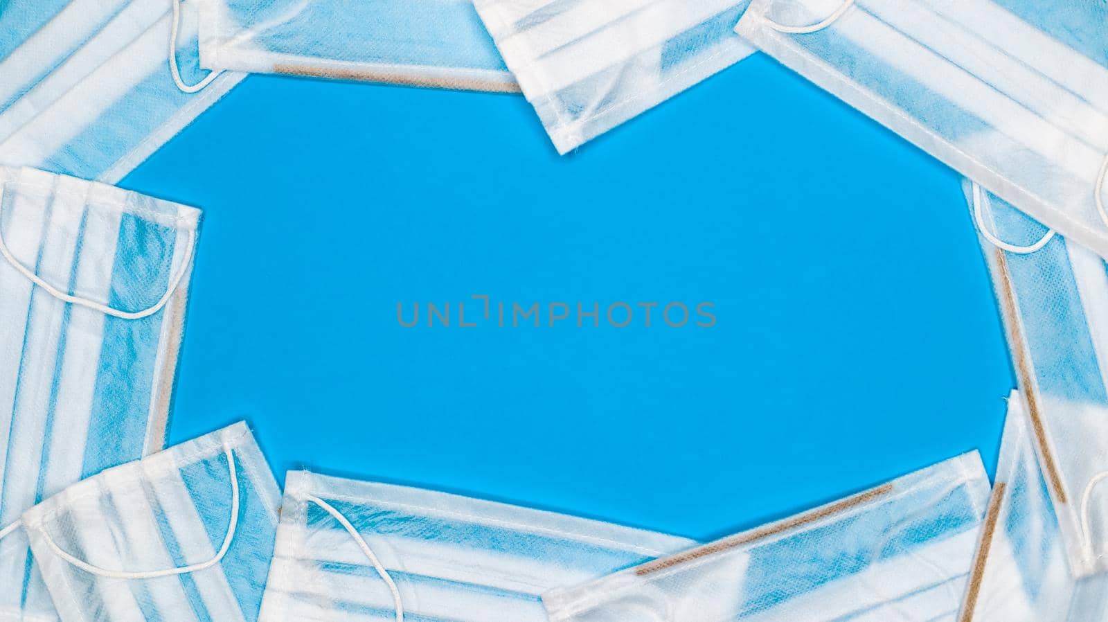 Many antiviral protective medical face masks with earloops are set against a blue background. Surgical mask background. Respiratory syndrome, coronavirus disease COVID-19. Copy space.