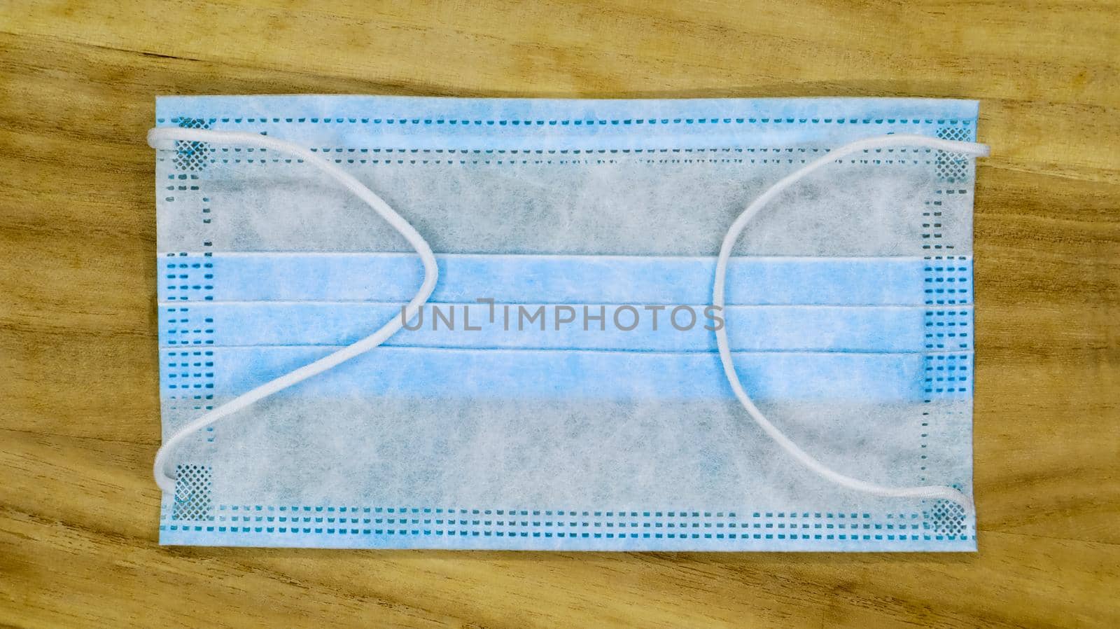 One 3-ply disposable surgical face mask with rubber pads covering the mouth and nose on a wooden table. The concept of protection from bacteria, healthcare and medicine. COVID-19. Dangerous virus