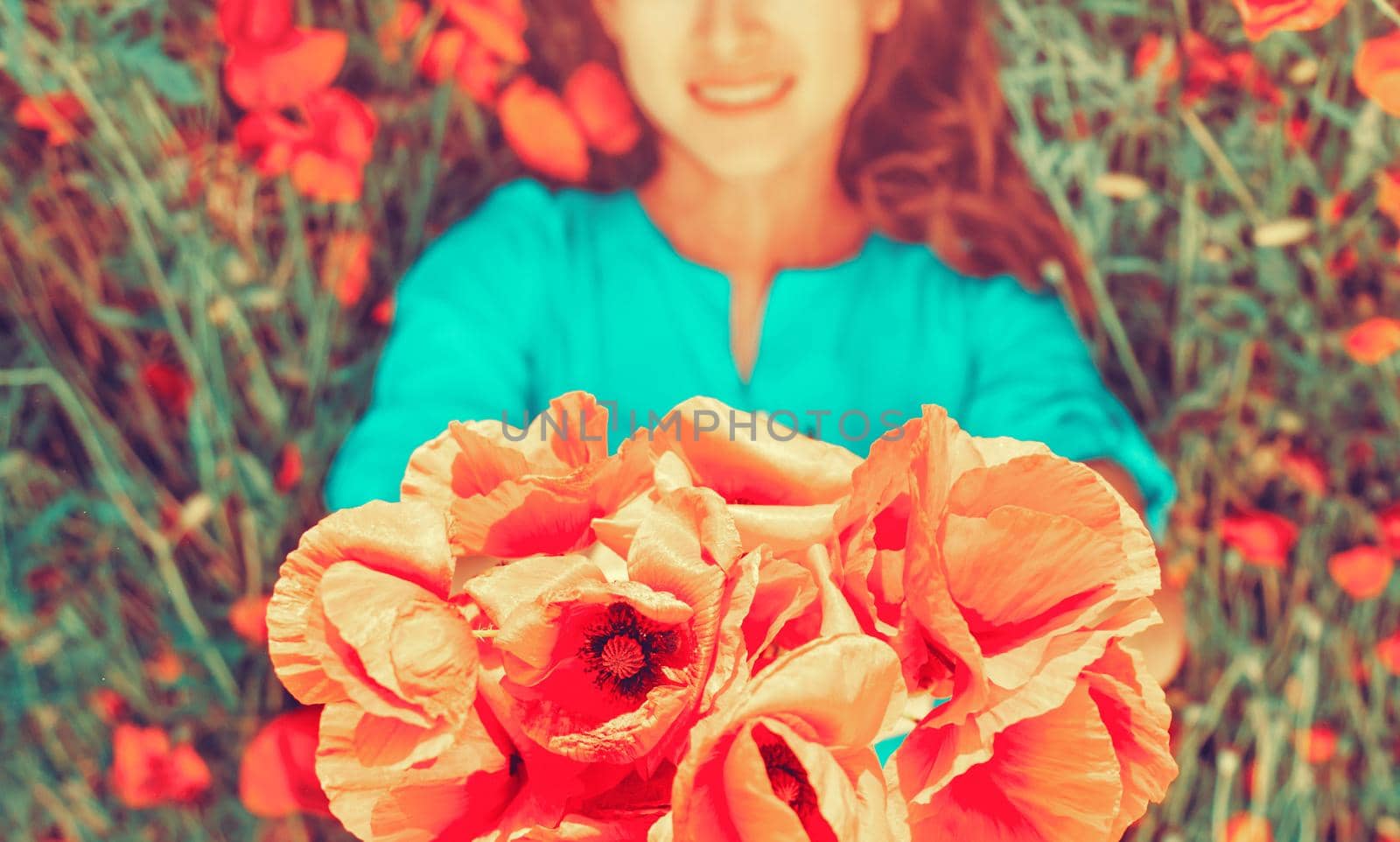 Smiling young woman lying with poppy bouquet on meadow, focus on flowers.