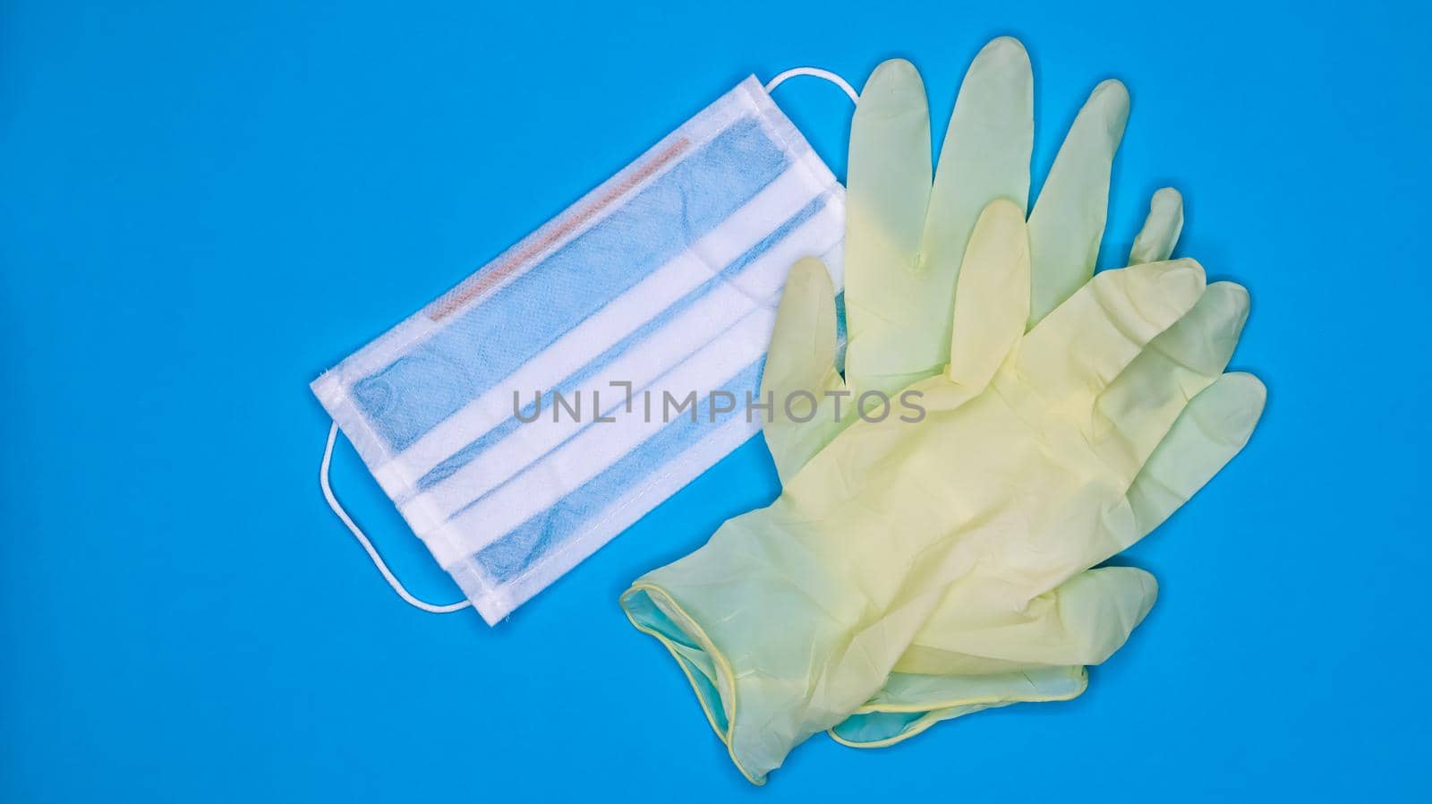 A pair of disposable latex medical gloves and a surgical mask on a blue background. Covid-19 virus protection concept. Protective items. Means of protection