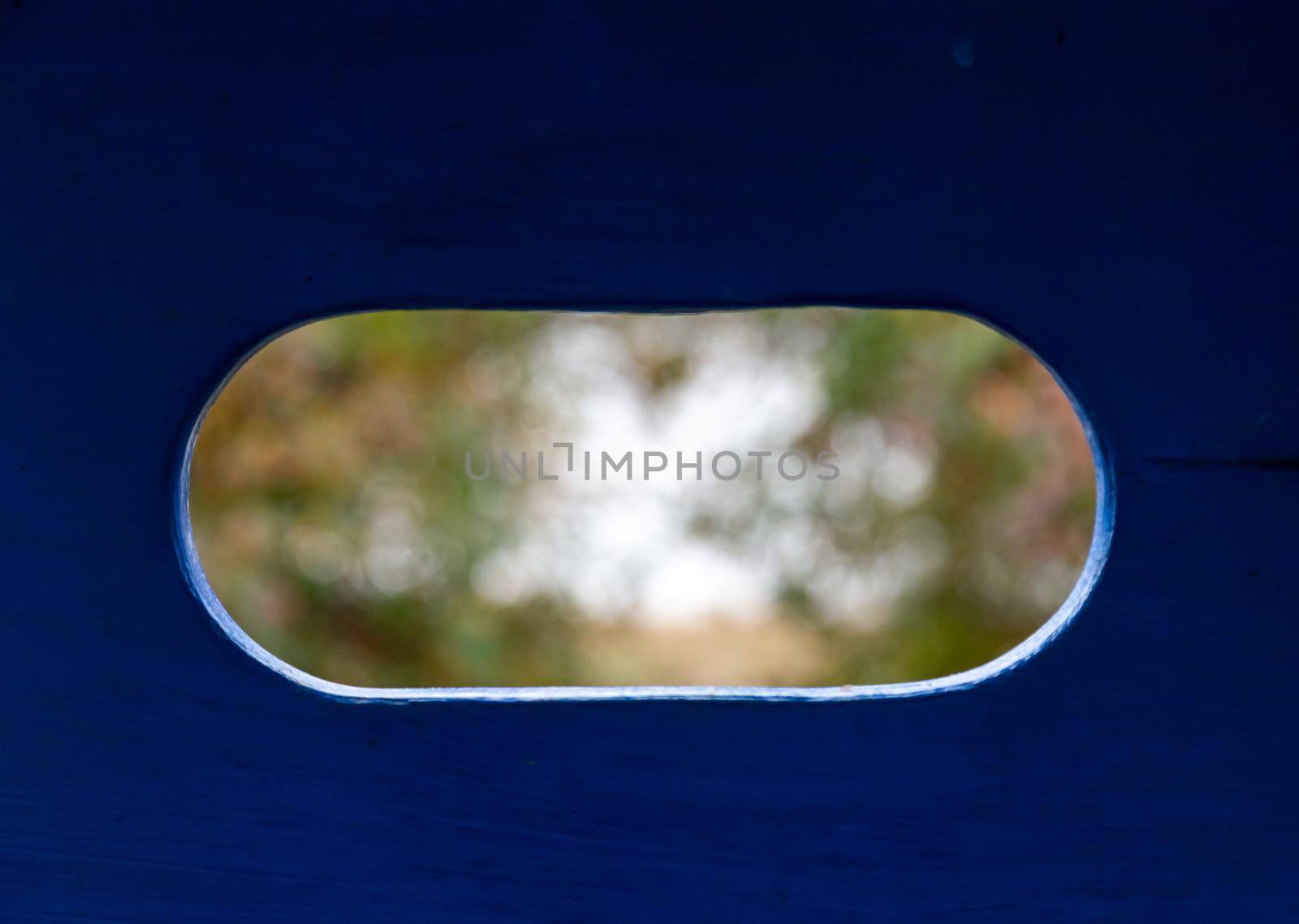 Blured Landscape, view of trees in the park through an oval hole in a blue wooden wall