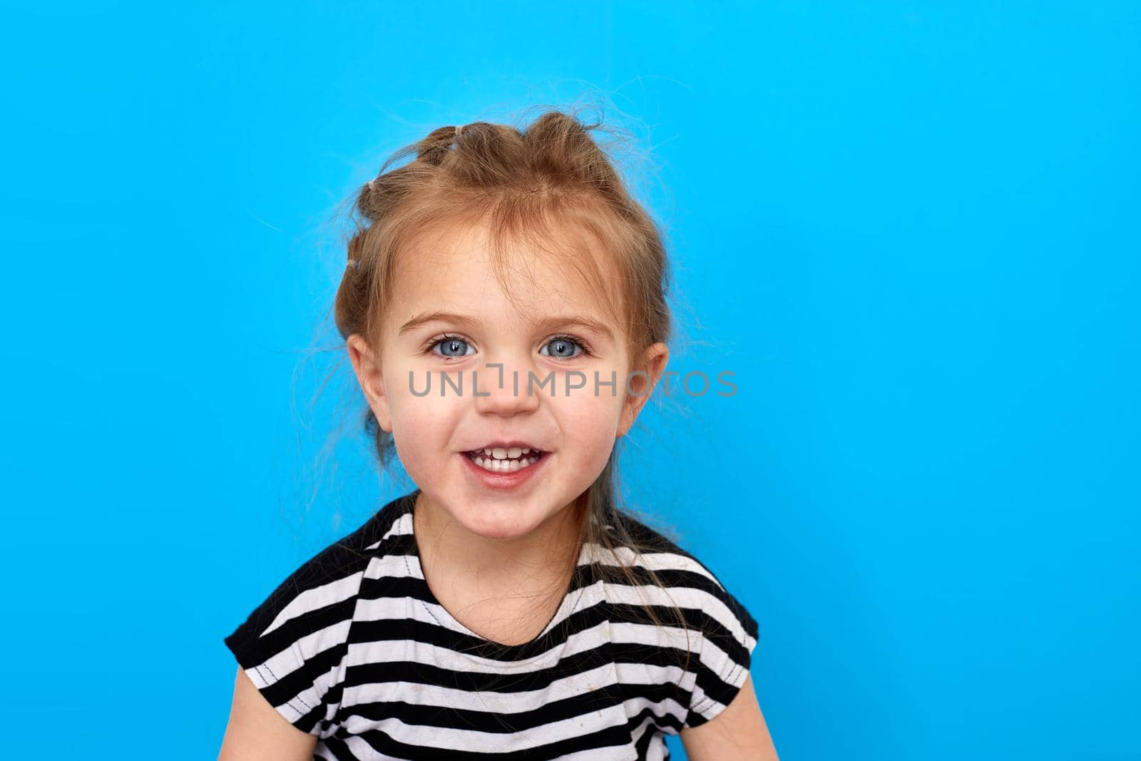 Close-up studio shot of a lovely little girl in t-shirt posing against a blue background. Looks at the camera and smiles