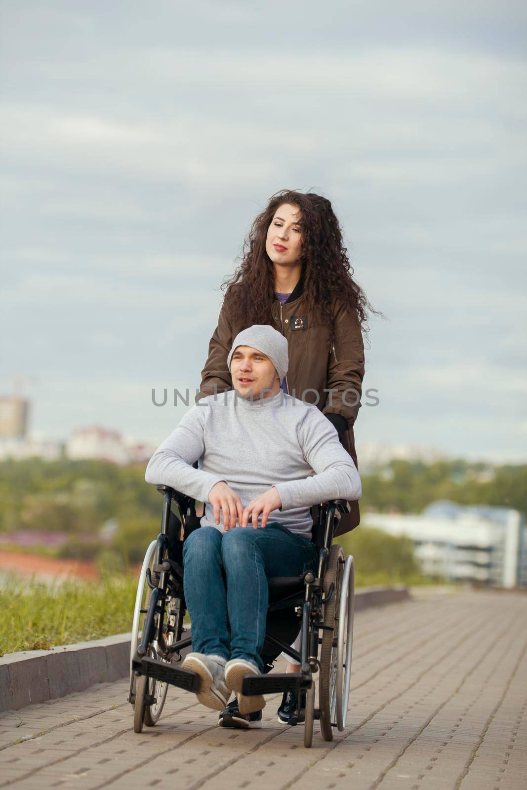 Disabled man in a wheelchair with young woman walking at the city street, close up