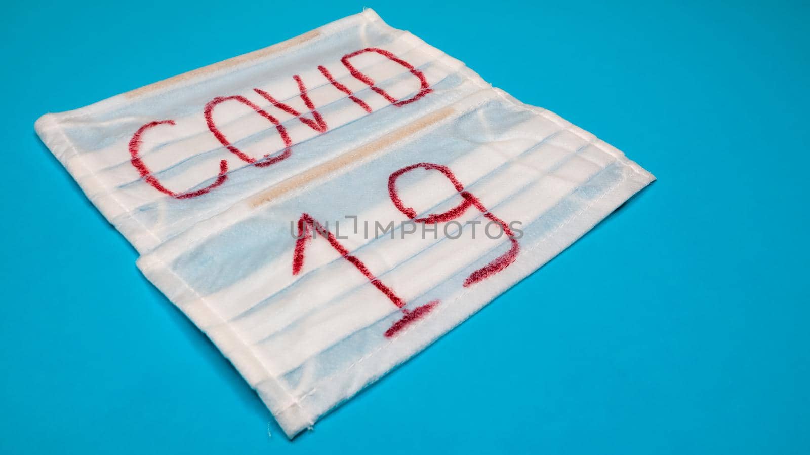 Typical white 3-ply surgical mask with rubber earhooks to cover mouth and nose with English block letters Covid-19 on a blue background. Dangerous virus and quarantine concept