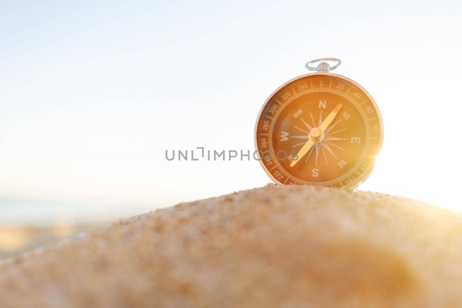 Compass on sand on sunny summer day, concept of travel and vacations. Copy-space in left part of image.