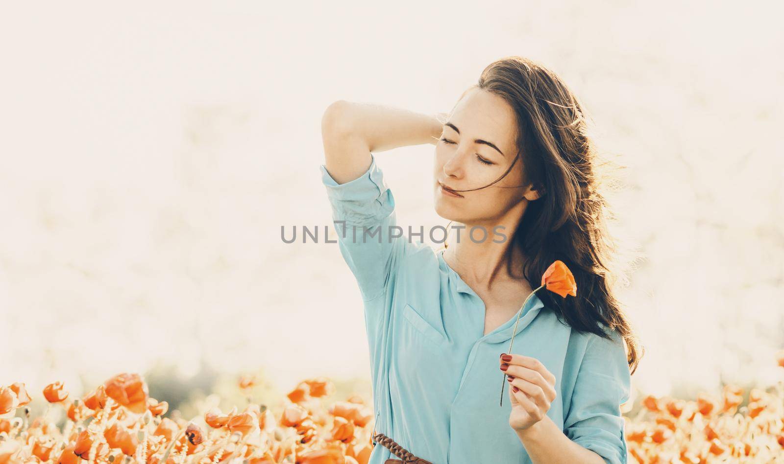 Outdoor portrait of pretty romantic young woman with poppy in spring. Brunette female with dreamy emotions relaxing in flower meadow.