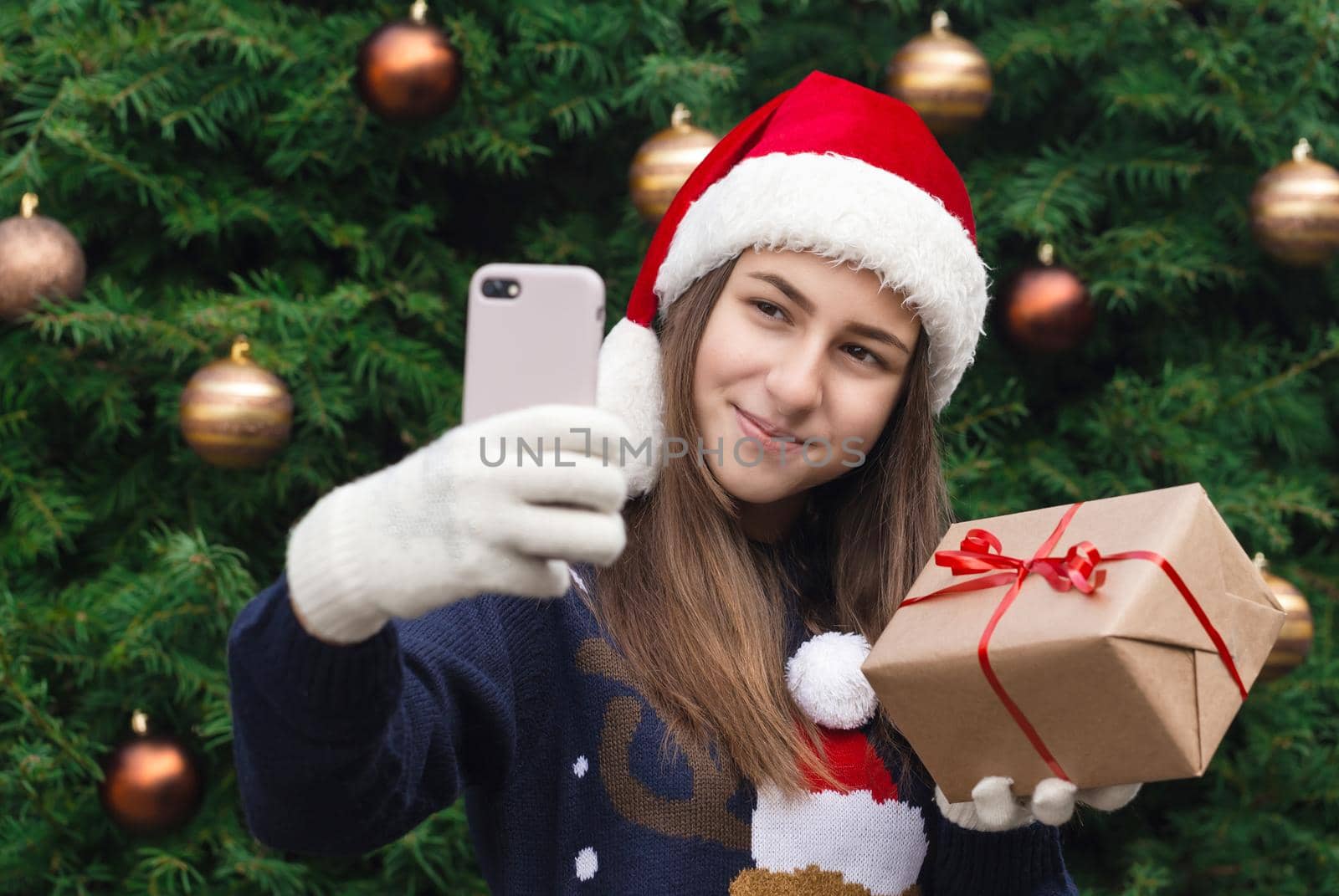 Christmas online greetings. girl in santa claus hat talks and using mobile smartphone for video call friends and parents. Christmas during coronavirus. by lunarts
