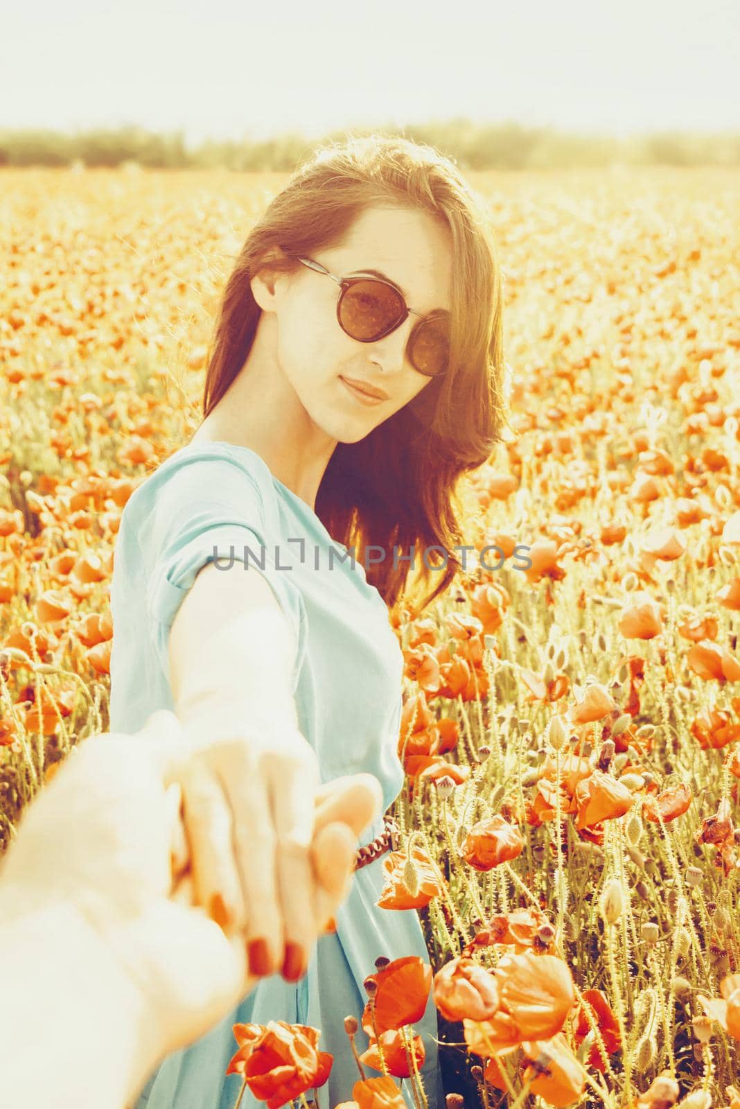 Attractive young woman holding male hand and leading him in poppies flowers meadow outdoor in spring, point of view.