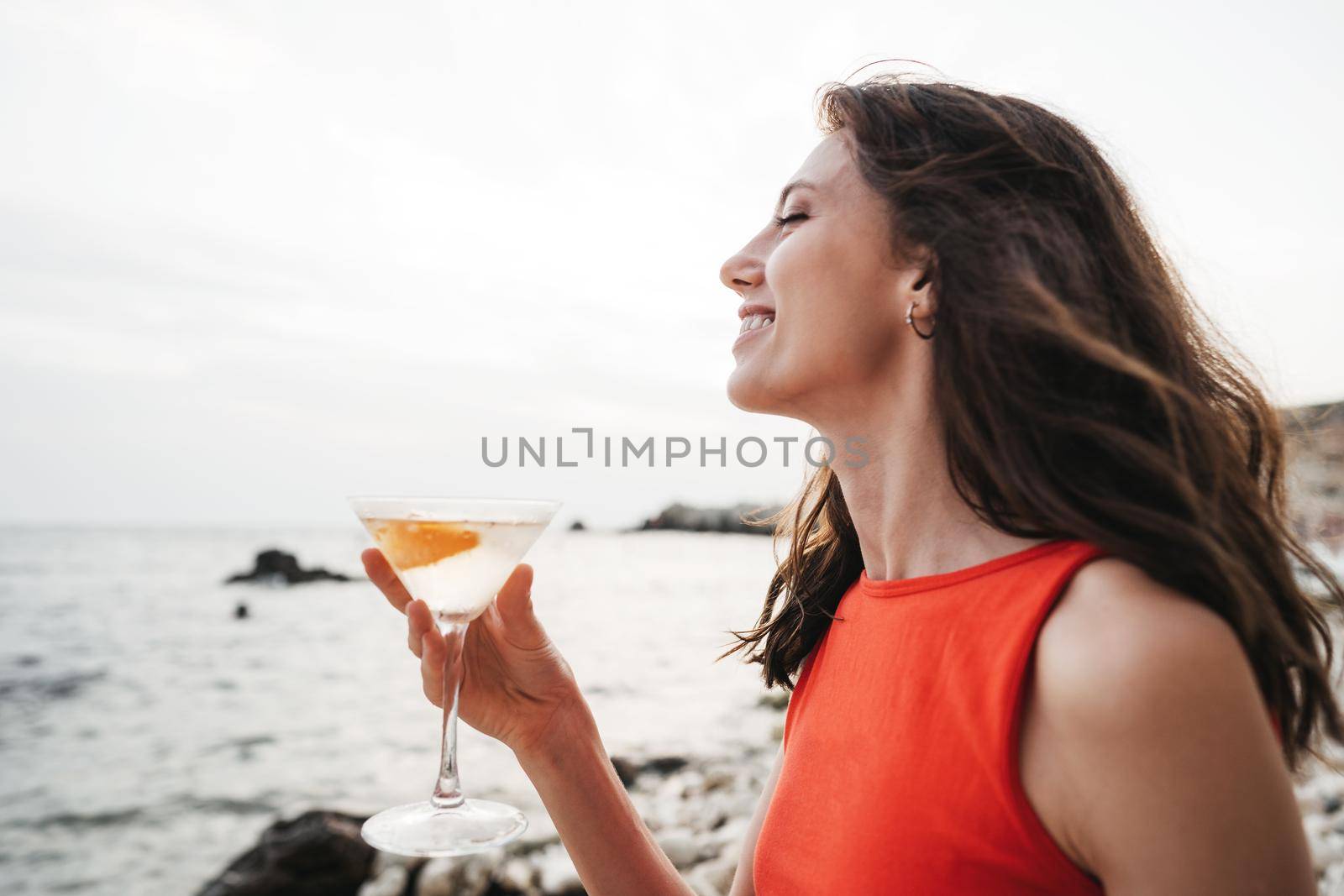 Portrait of young woman with cocktail glass chilling on a beach, close up