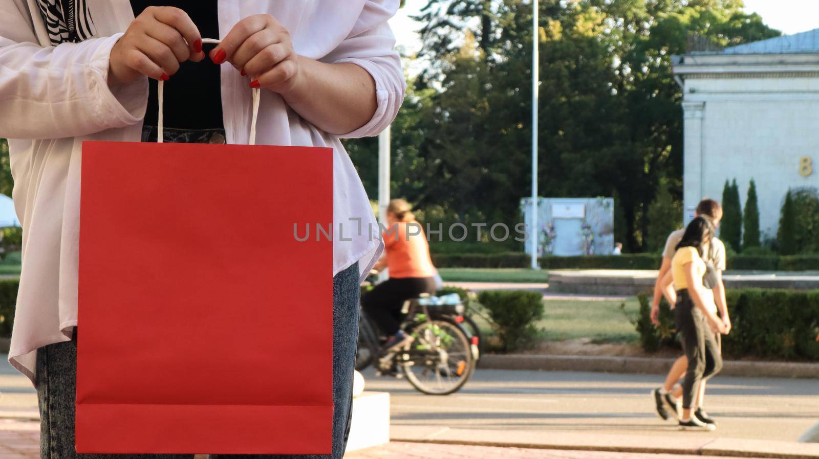 Close-up of a shopaholic woman with a red paper shopping bag in her hands. Crop the photo. Consumerism, shopping, lifestyle concept. Copy space for your logo. Black Friday by Roshchyn