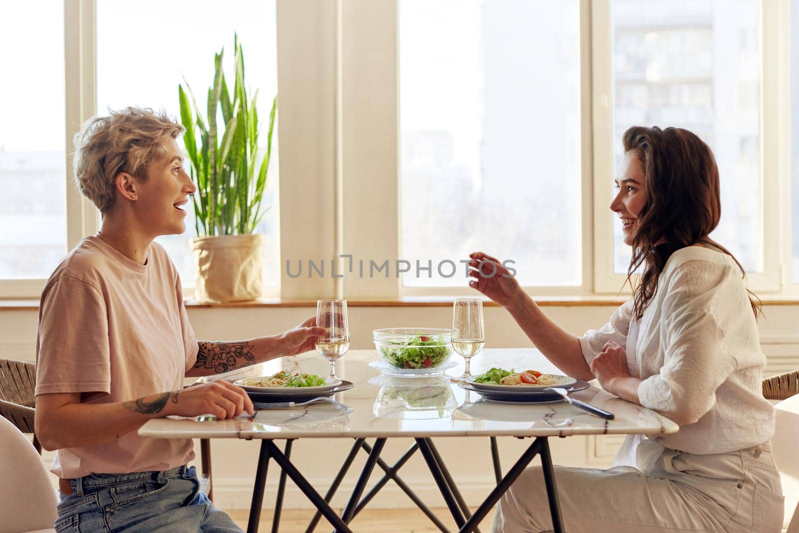 Smiling couple enjoying dinner meal sitting at kitchen table together and drinking white wine healthy eating