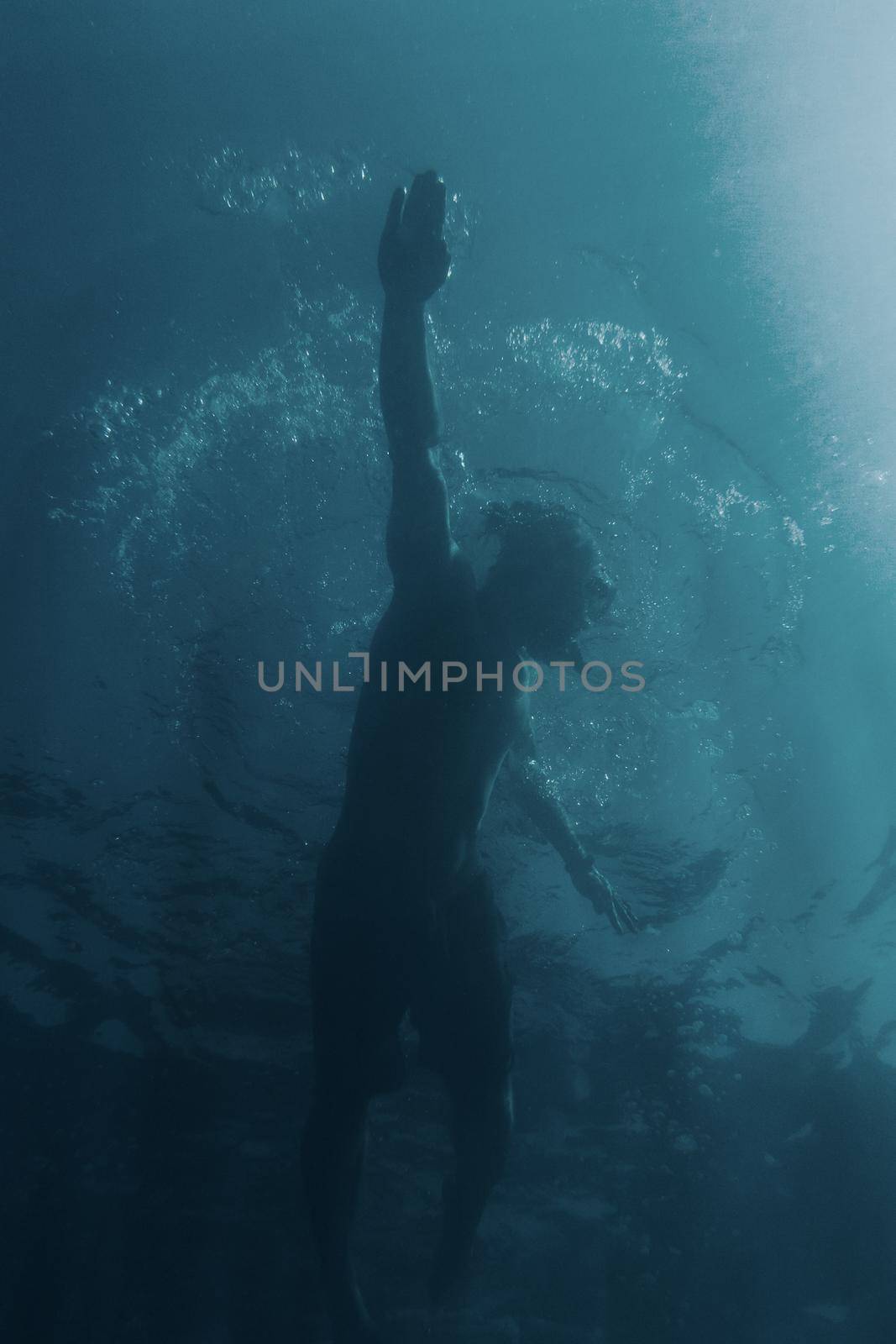 Young man swimming underwater and using crawl technique, bottom view.