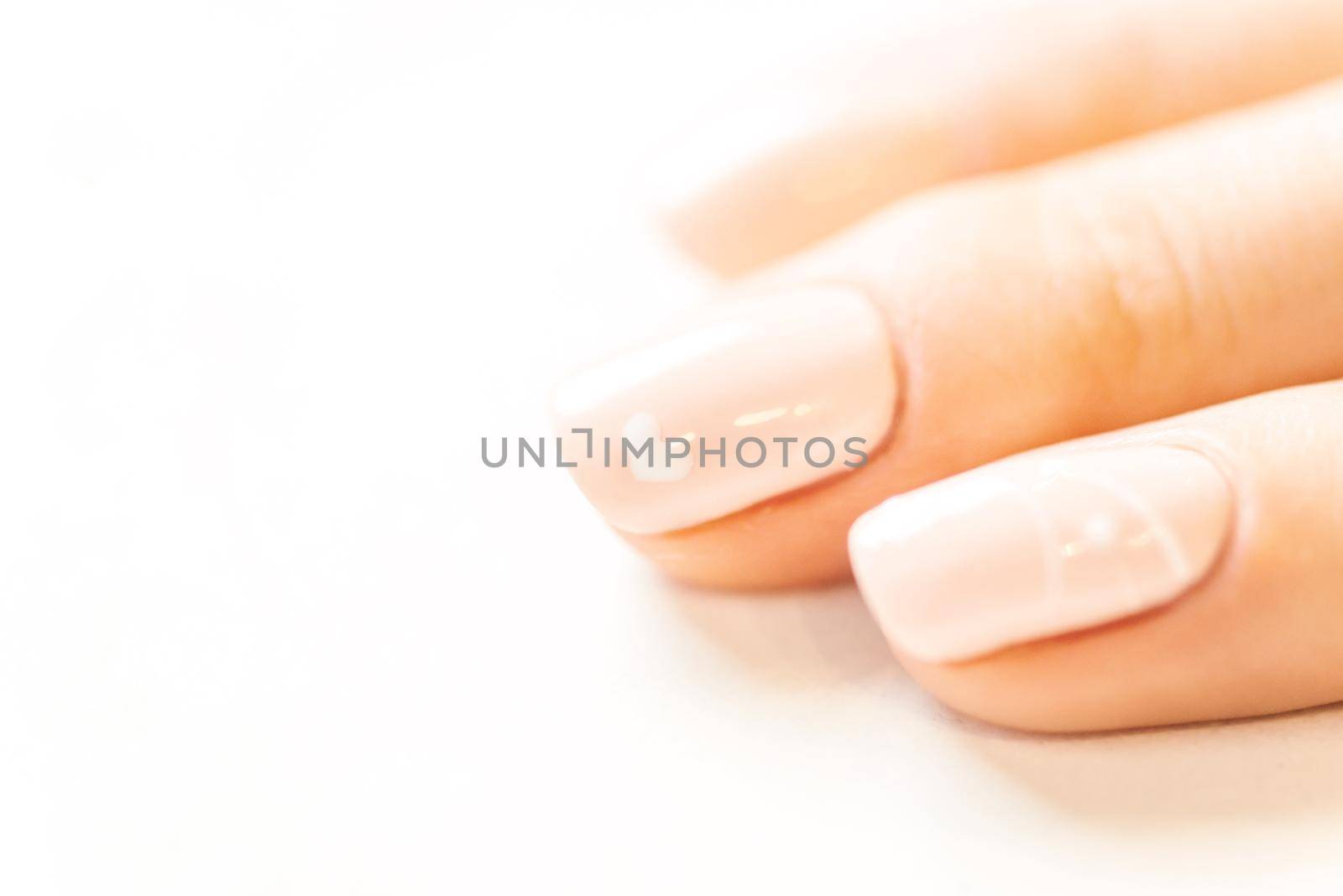 Female fingers with professional manicure and natural beige color polish, close-up.