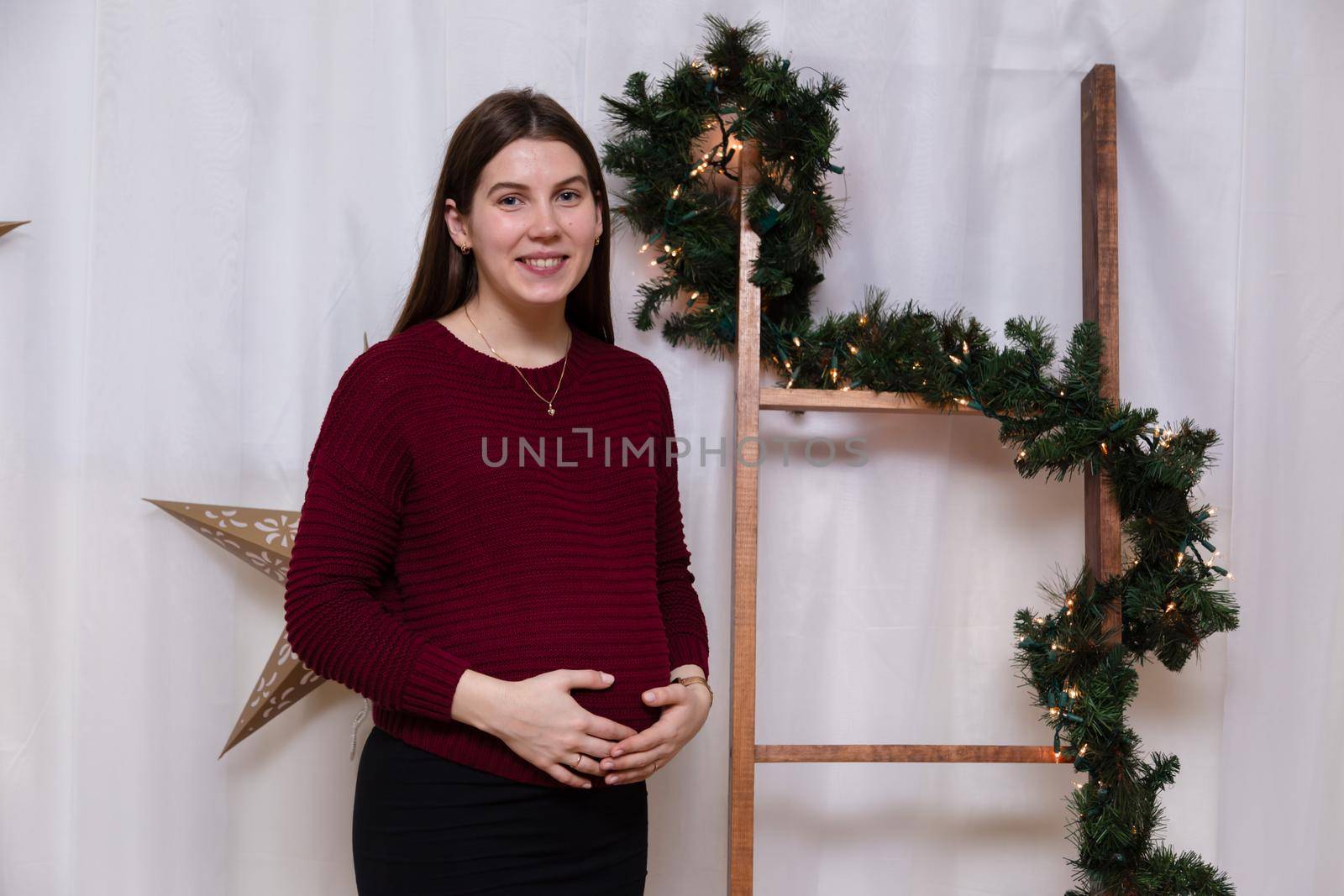 beautiful smiley pregnant girl standing on the background of christmas decoration. Christmas or New Year atmosphere.