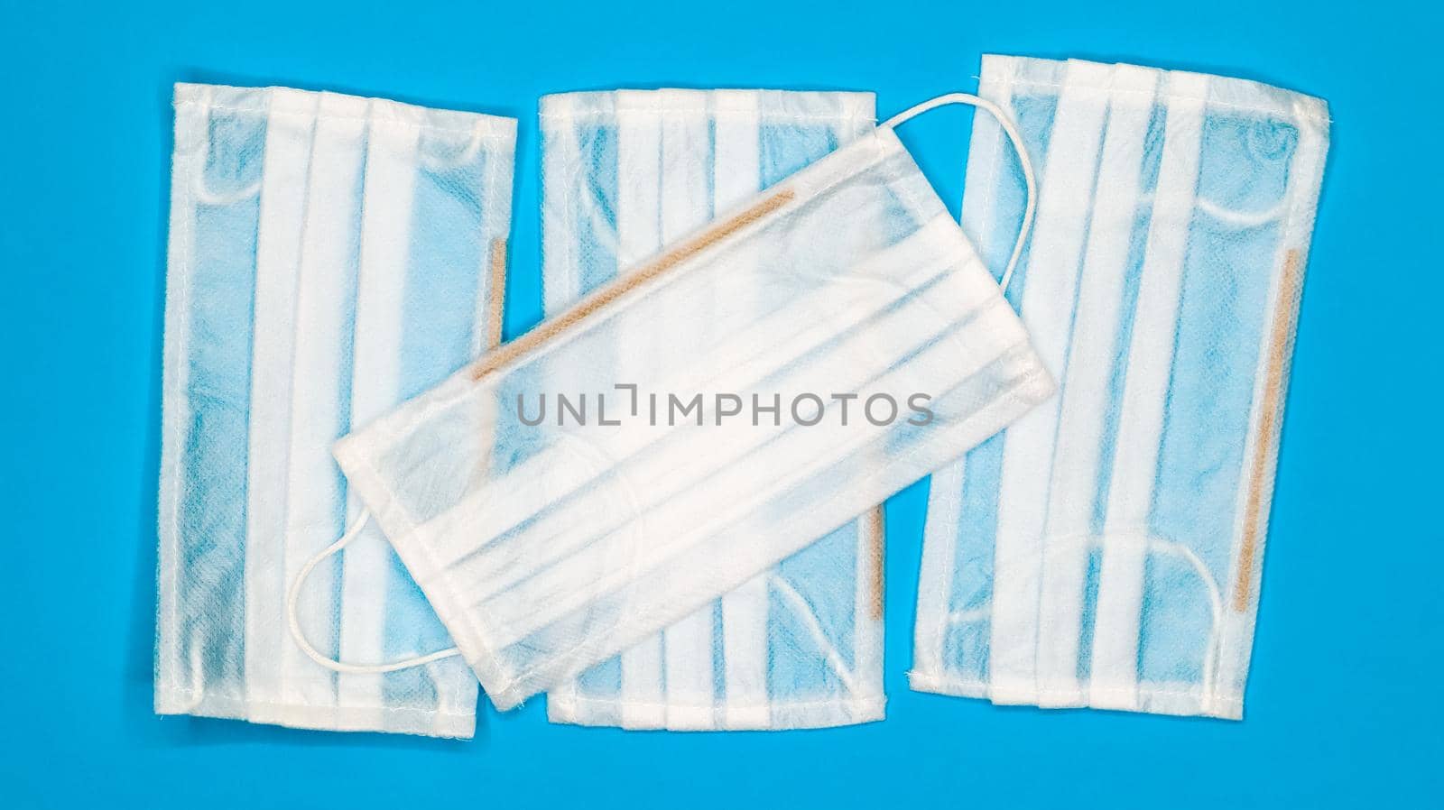 Four disposable surgical face masks with rubber pads to cover the mouth and nose on a blue background. The concept of protection from bacteria, healthcare and medicine. COVID-19. Dangerous virus.