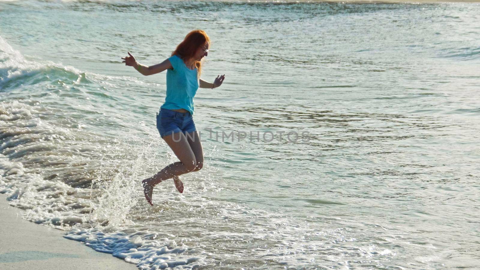 Young woman with long red hair play with waves running, feeling the sea, seascape beach of Dominican Republic, Caribbean sea