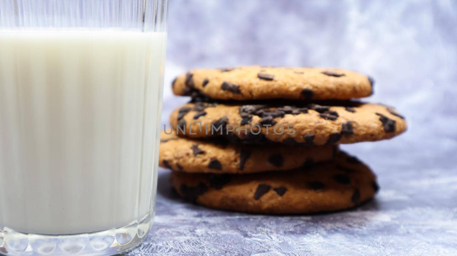 American chocolate chip cookies stacked on top of each other with milk in a glass on a gray background. Traditional rounded crunchy dough with chocolate chips. Bakery. Delicious dessert, pastries