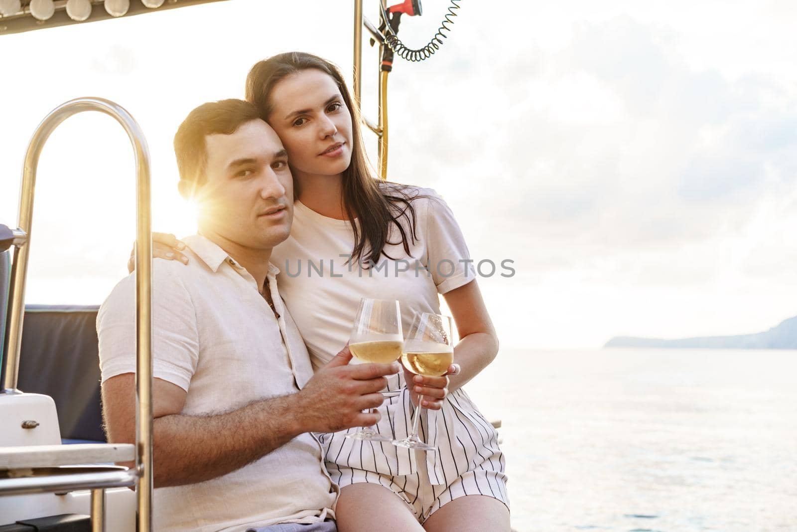 Young loving couple sitting on the yacht deck and drinking wine together