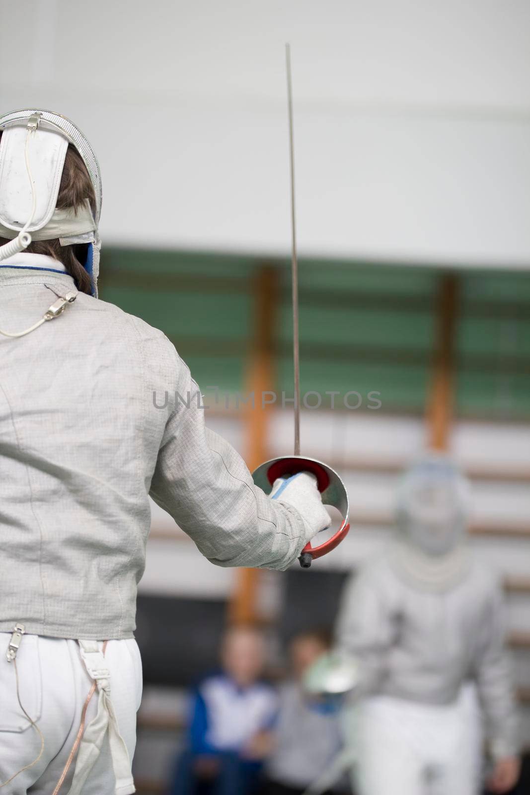 Two teenager fencers fighting with rapiers on the fencing tournament, telephoto shot