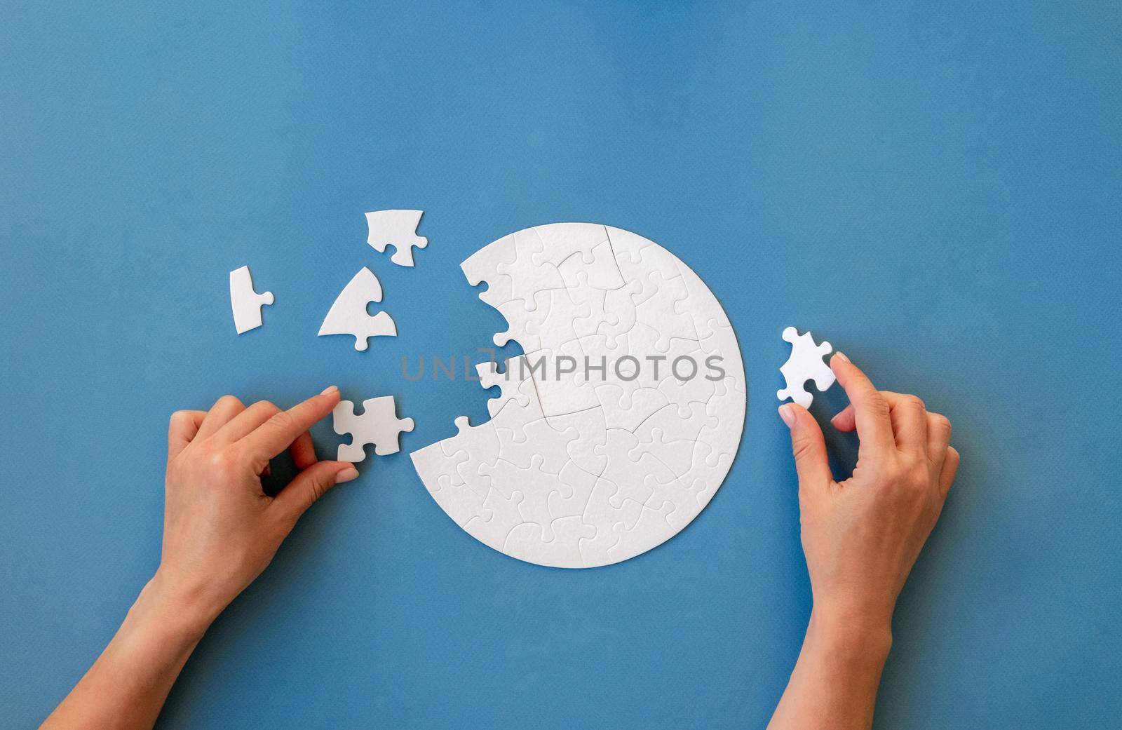 Hand putting last piece in white round shaped jigsaw puzzle on blue background