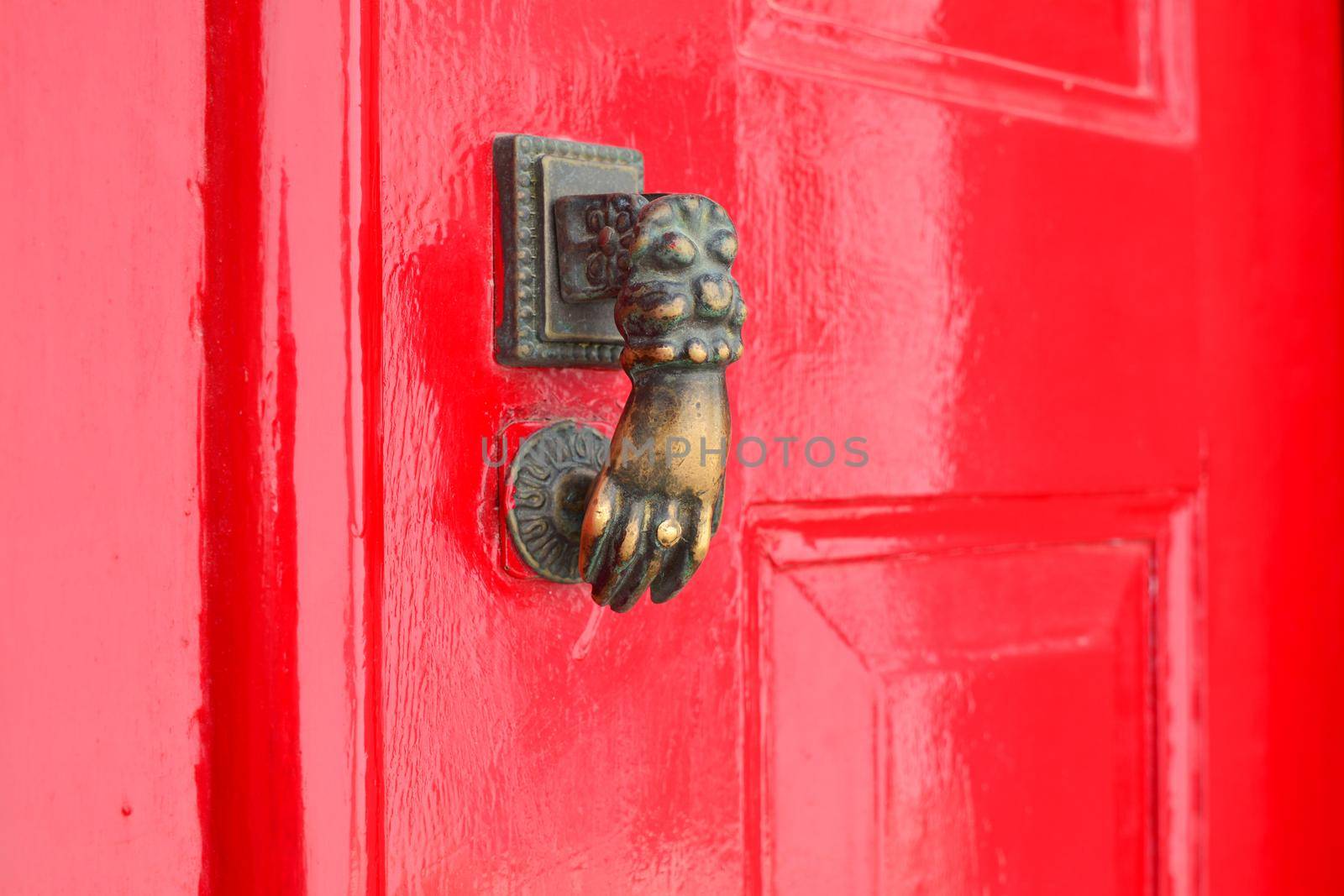 Red lacquered door with doorknocker Metal arm of woman