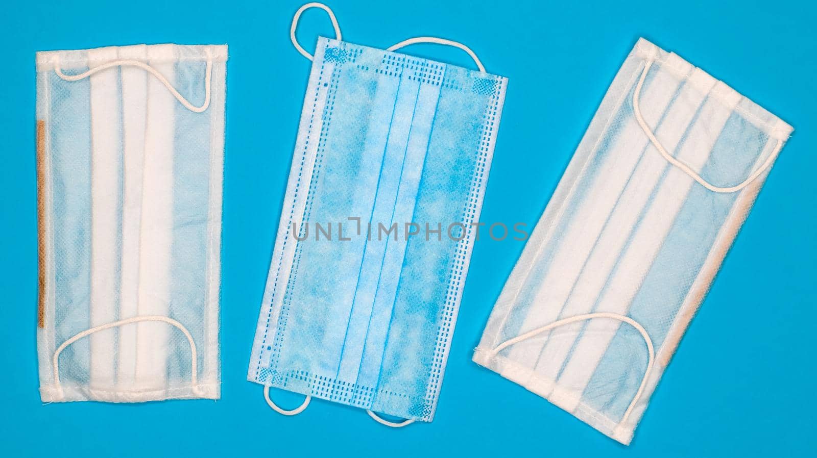 Three disposable surgical face masks with rubber pads to cover the mouth and nose on a blue background. The concept of protection from bacteria, healthcare and medicine. COVID-19. Dangerous virus.