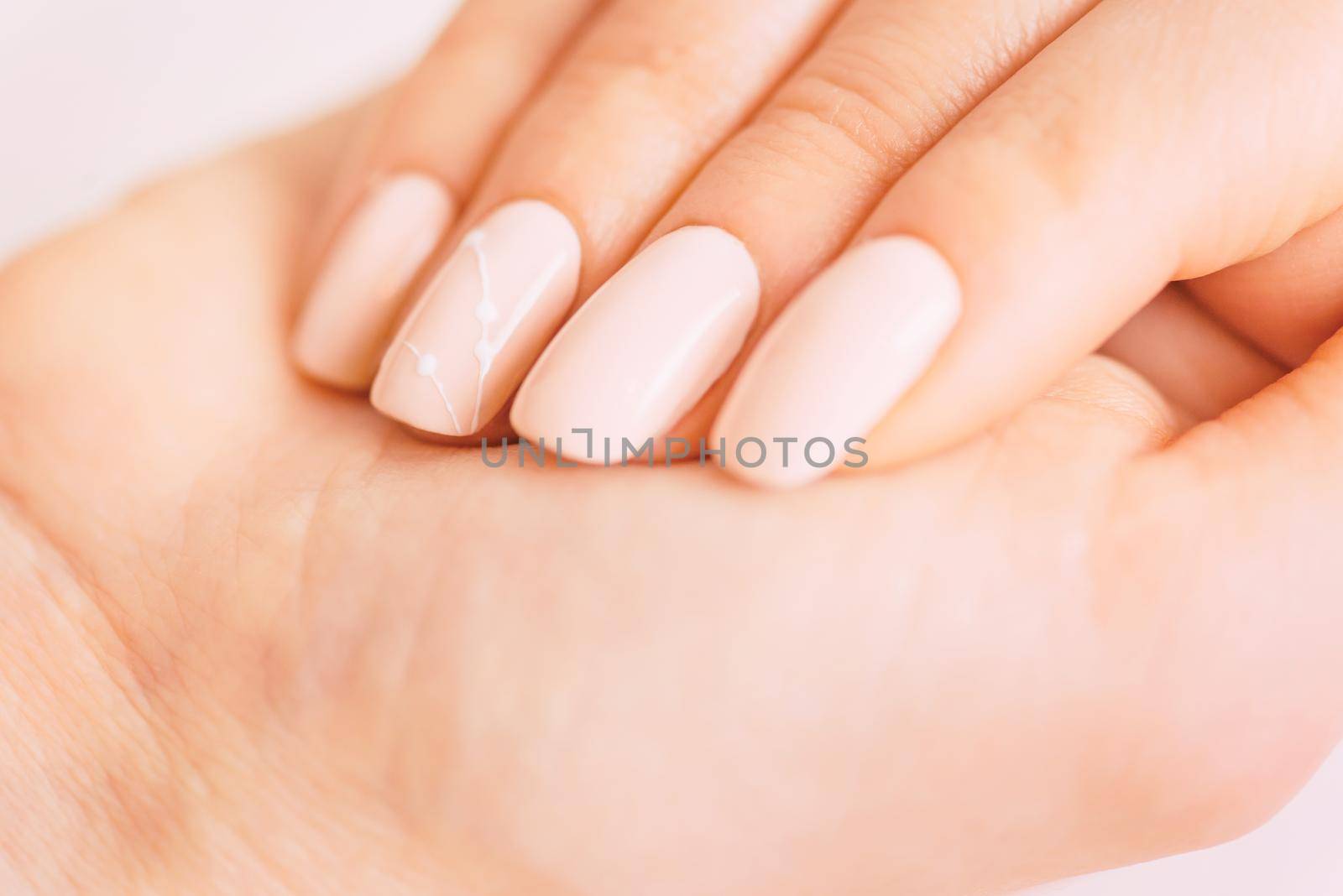 Female hand with professional manicure of beige natural color and art design. Concept of beauty salon.