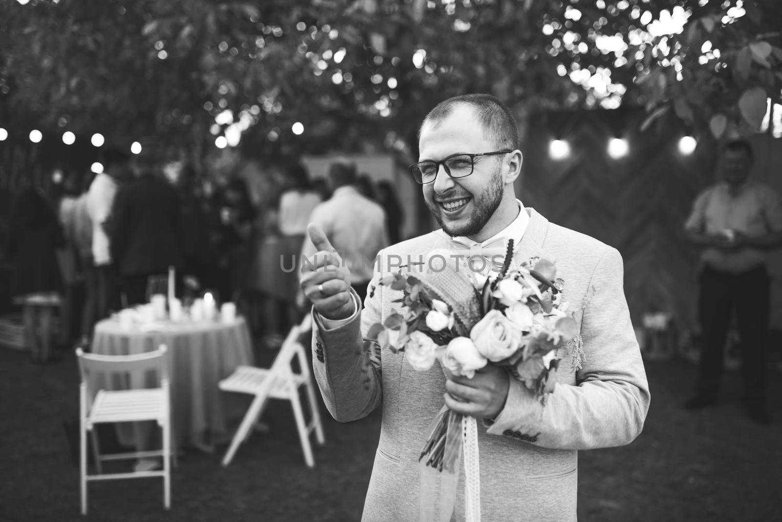 Wedding photo of emotions of a bearded groom with glasses in a gray jacket and rustic style.