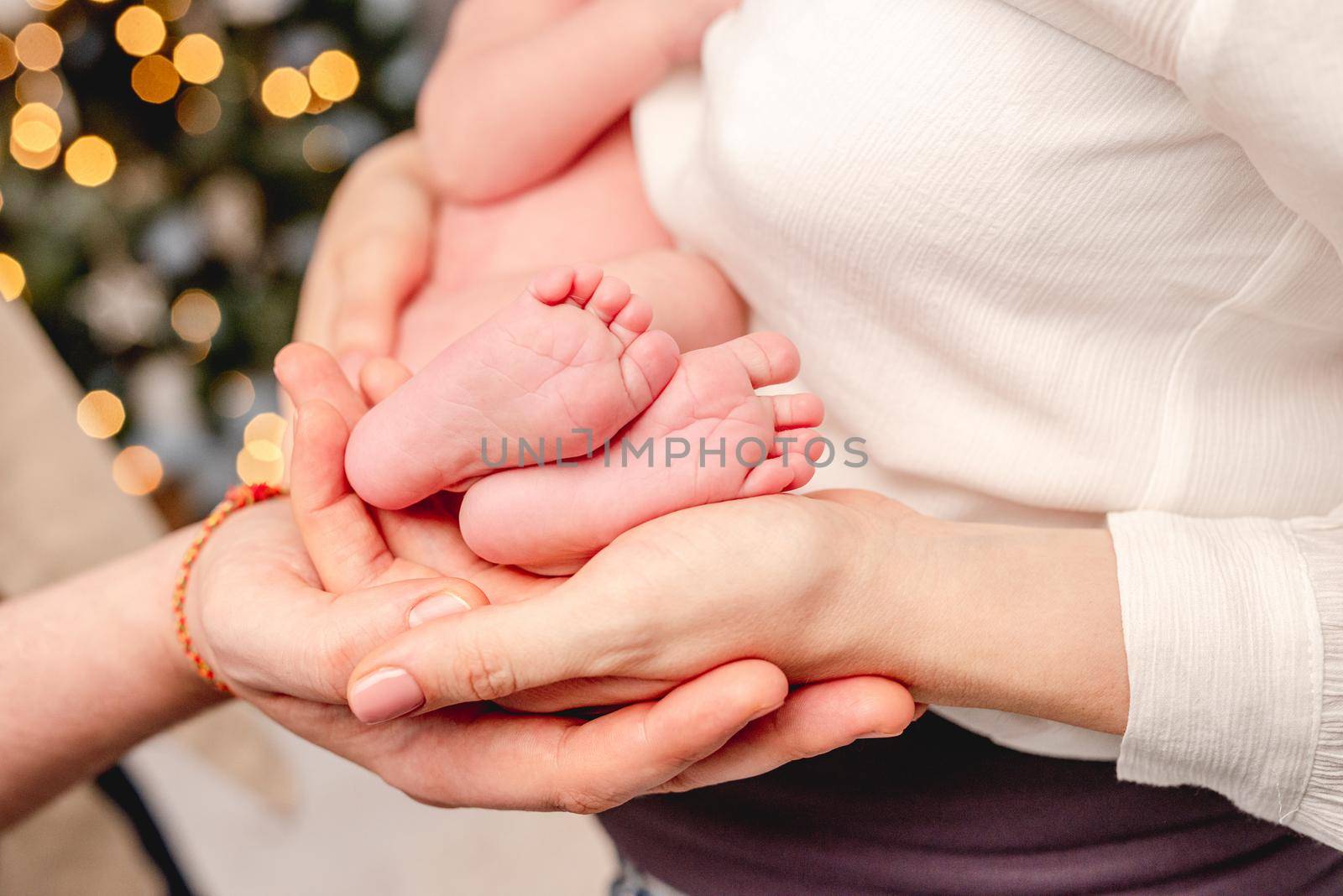 Bare feet of newborn baby surrounded by family members hands