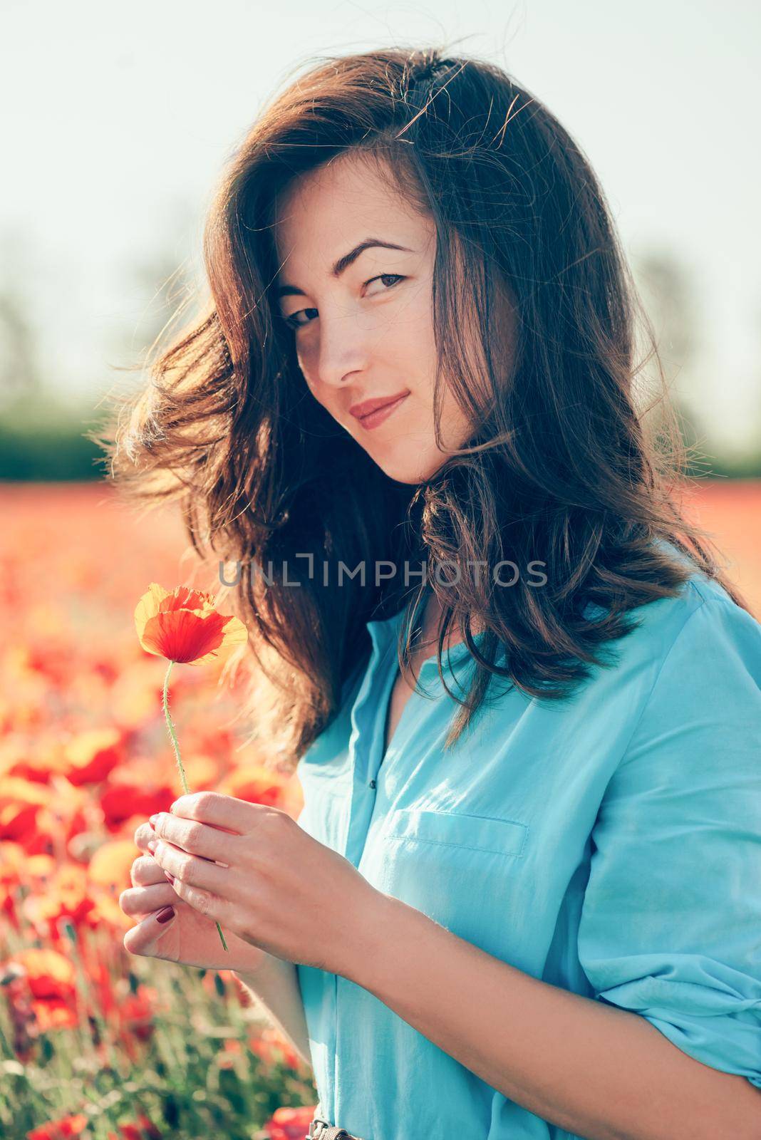 Beautiful young woman holding poppy flower and looking at camera in spring meadow outdoor.