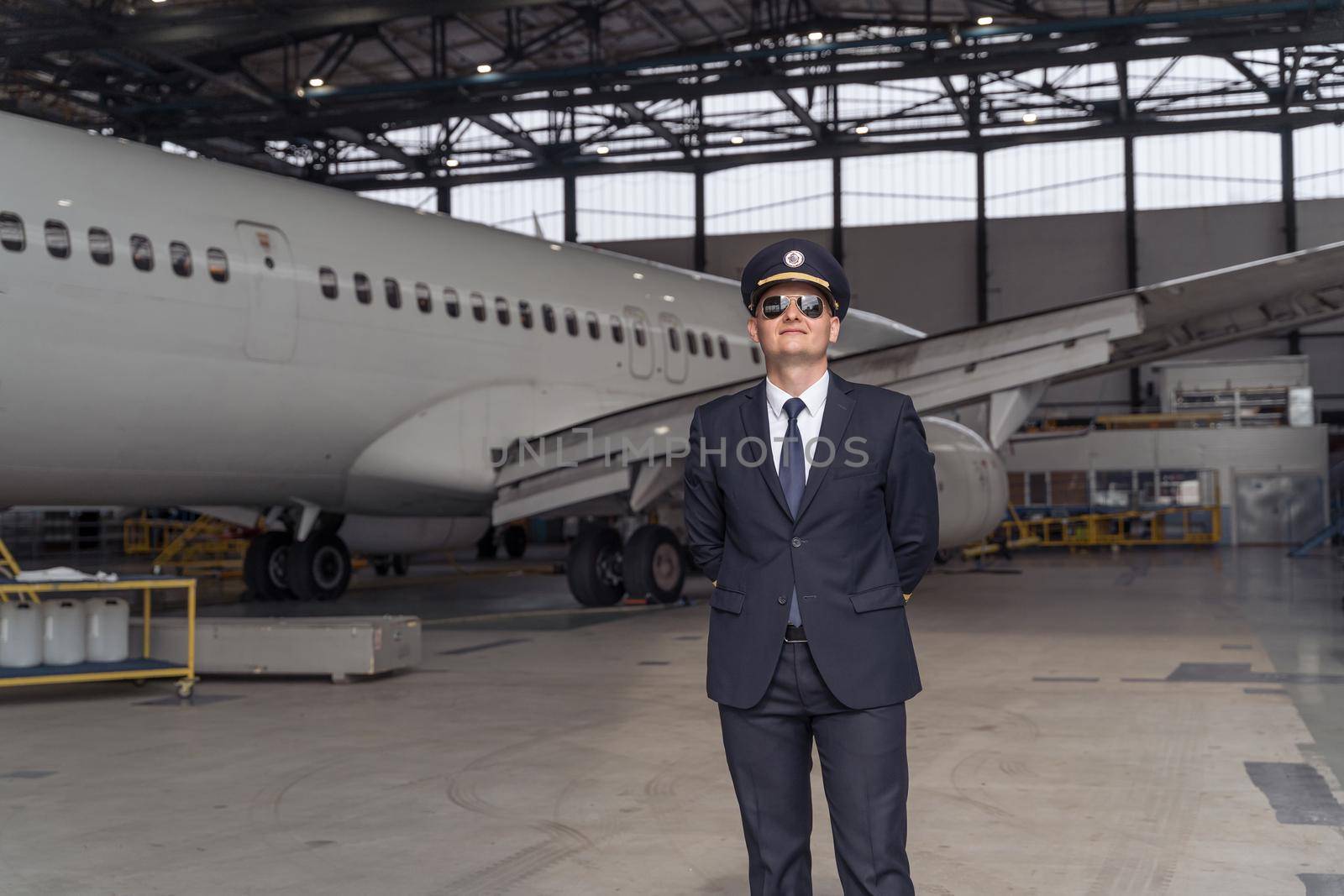 Pilot wearing sunglasses ready for flight while standing in front of big passenger airplane in airport