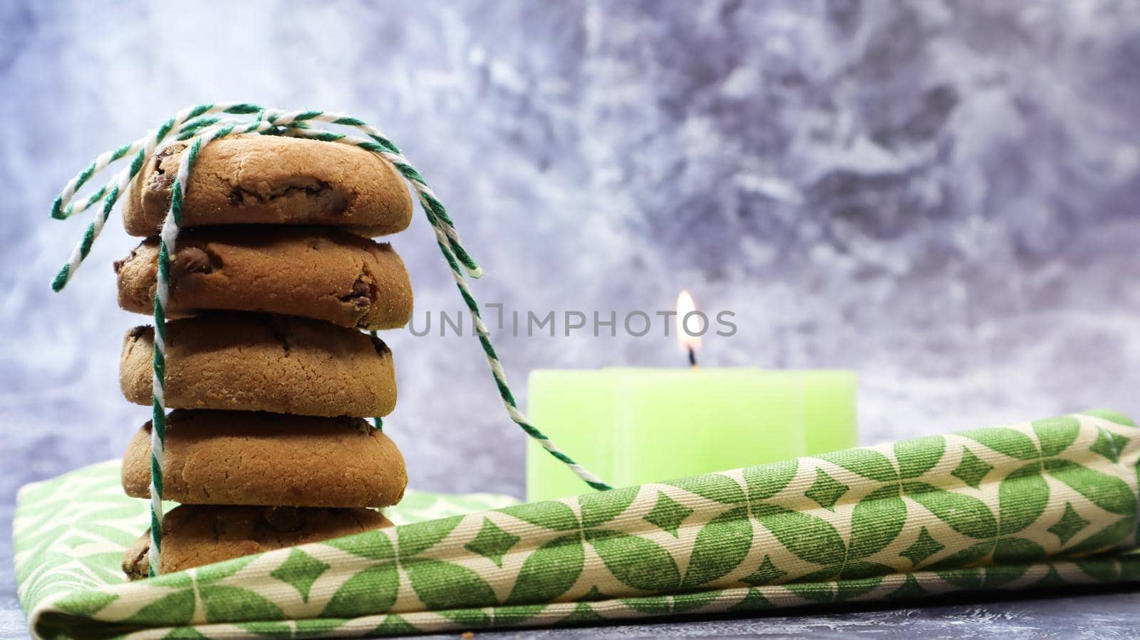 American chocolate chip cookies in a stack tied with thread on a green napkin and a candle. Traditional rounded crunchy dough with chocolate chips. Bakery. Delicious dessert, pastries