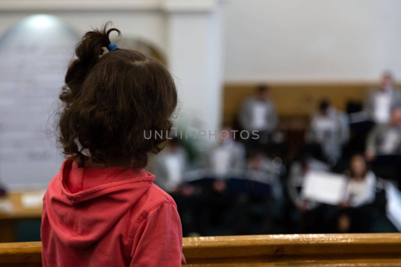 A view from the back of a little girl in a red sweater, who is looking at an orchestra that is out of focus