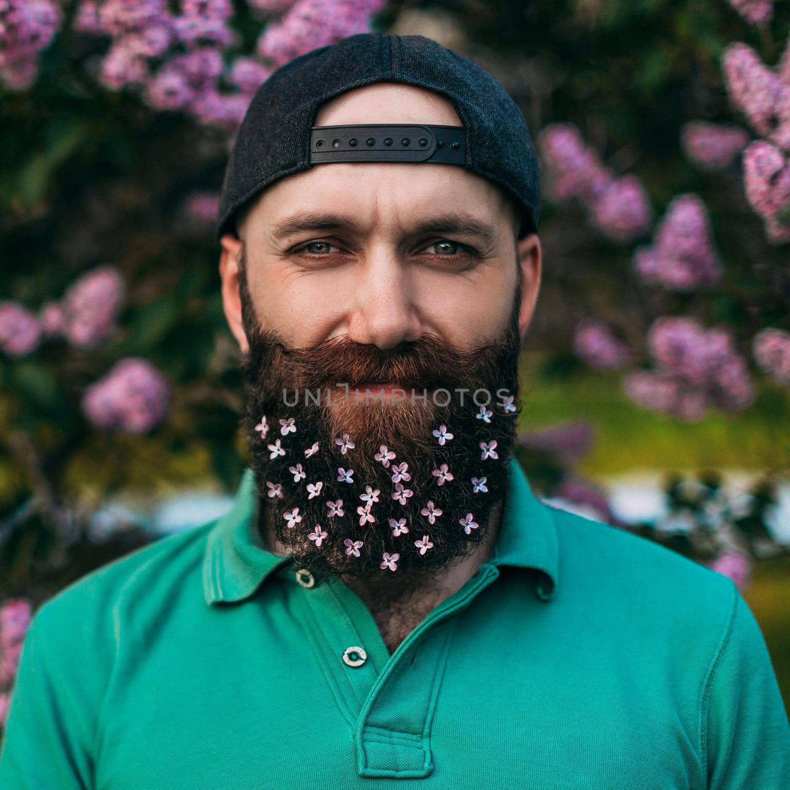 A bearded man with a decorated beard for the Spring holiday. Lilac flowers in the beard.